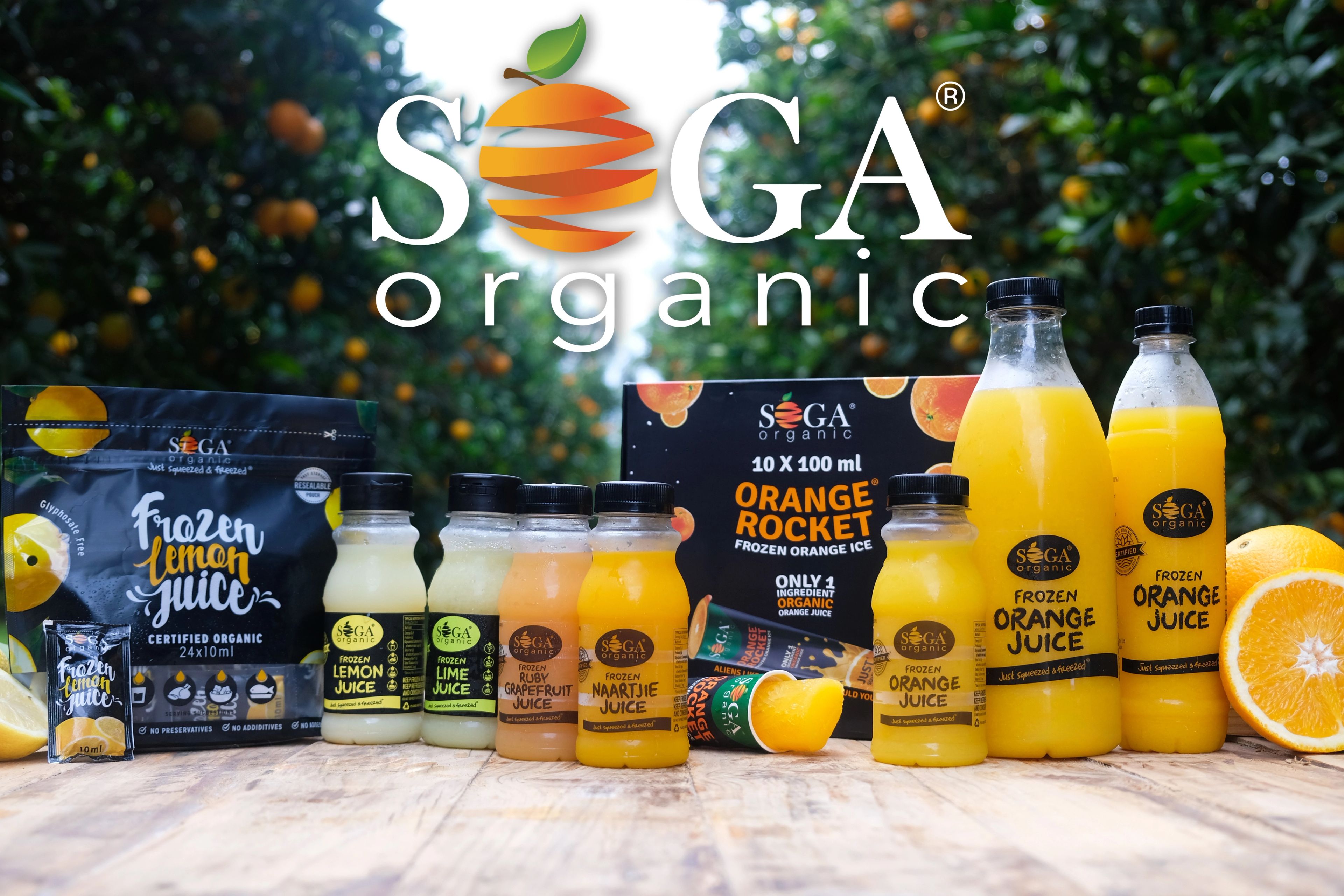 The full SOGA Organic frozen juice range on a wooden table in a citrus orchard, with the SOGA Organic logo above