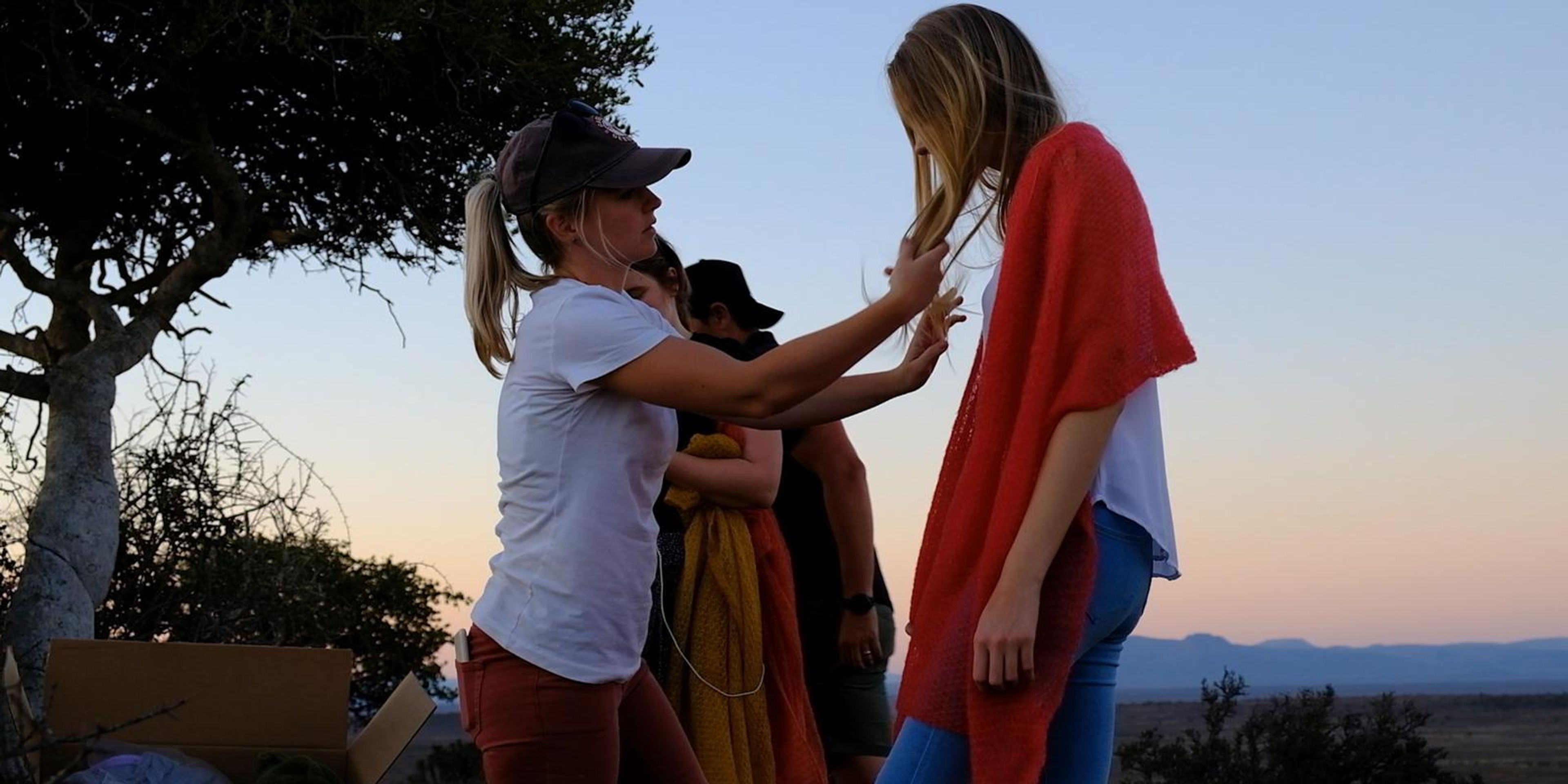 Stylist adjusting the model's hair beside a bright orange wrap