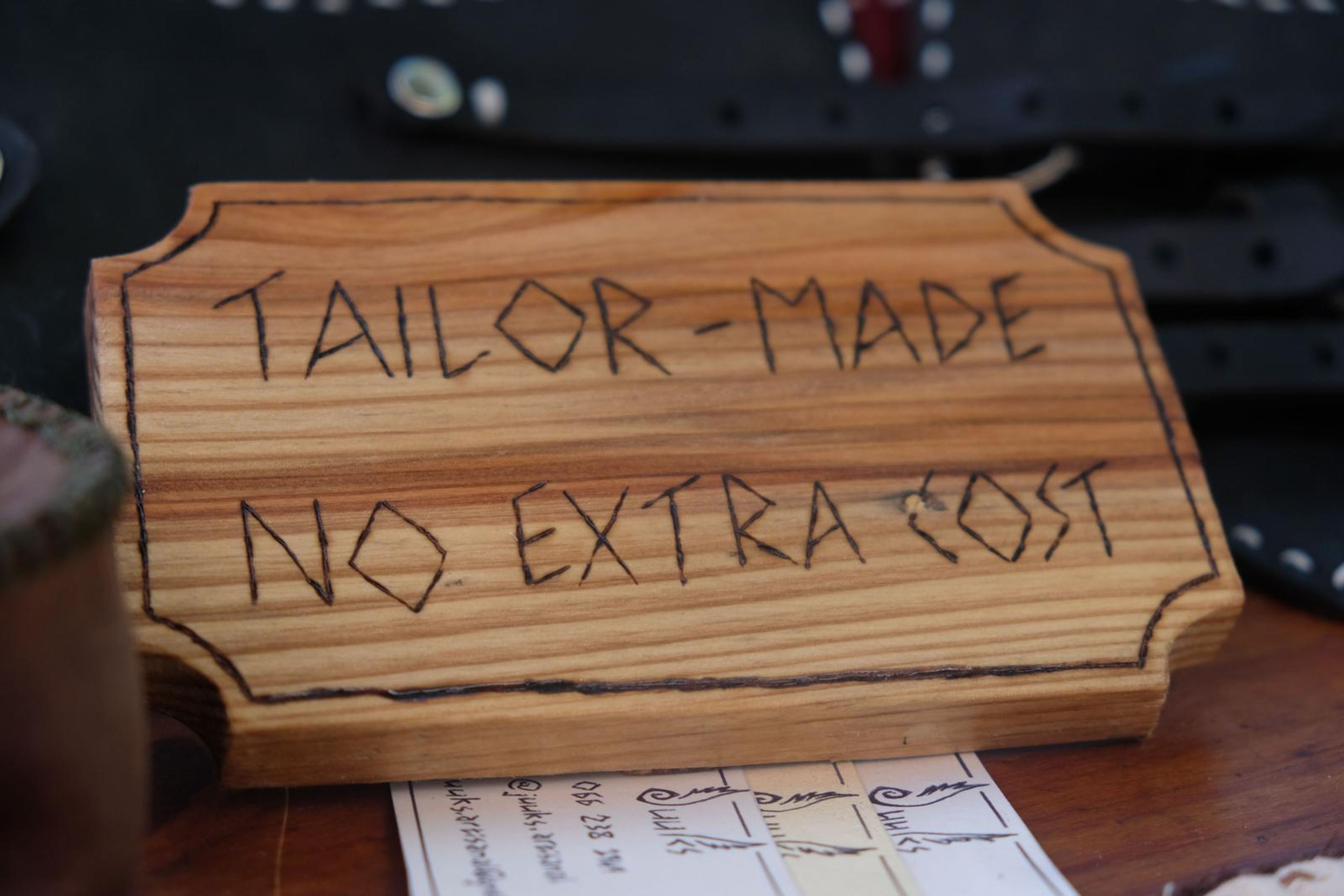 Black leather pouch and corset belts beside a Tailor-Made No Extra Cost sign