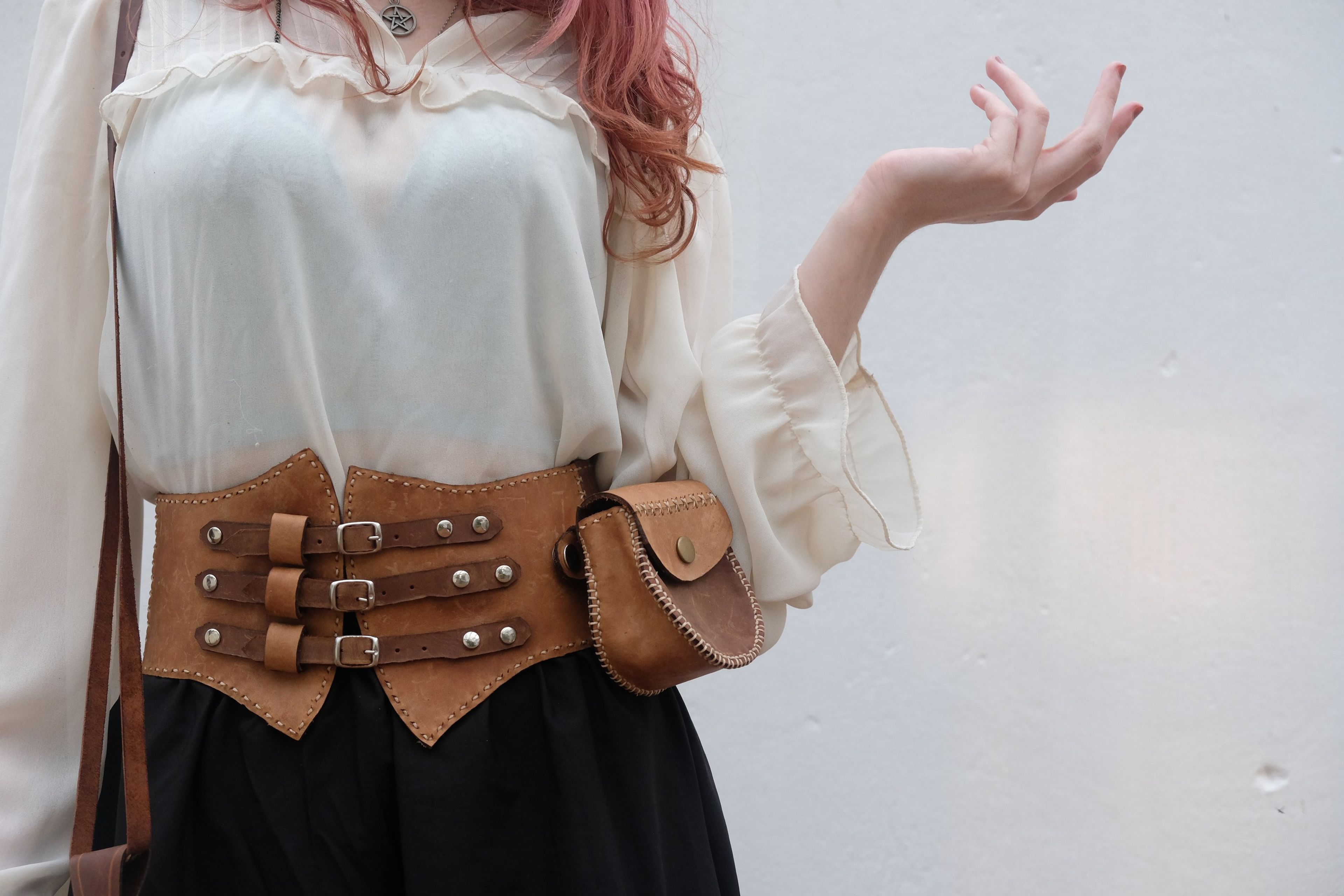 Woman in a cream blouse with her hand raised, wearing a leather corset belt