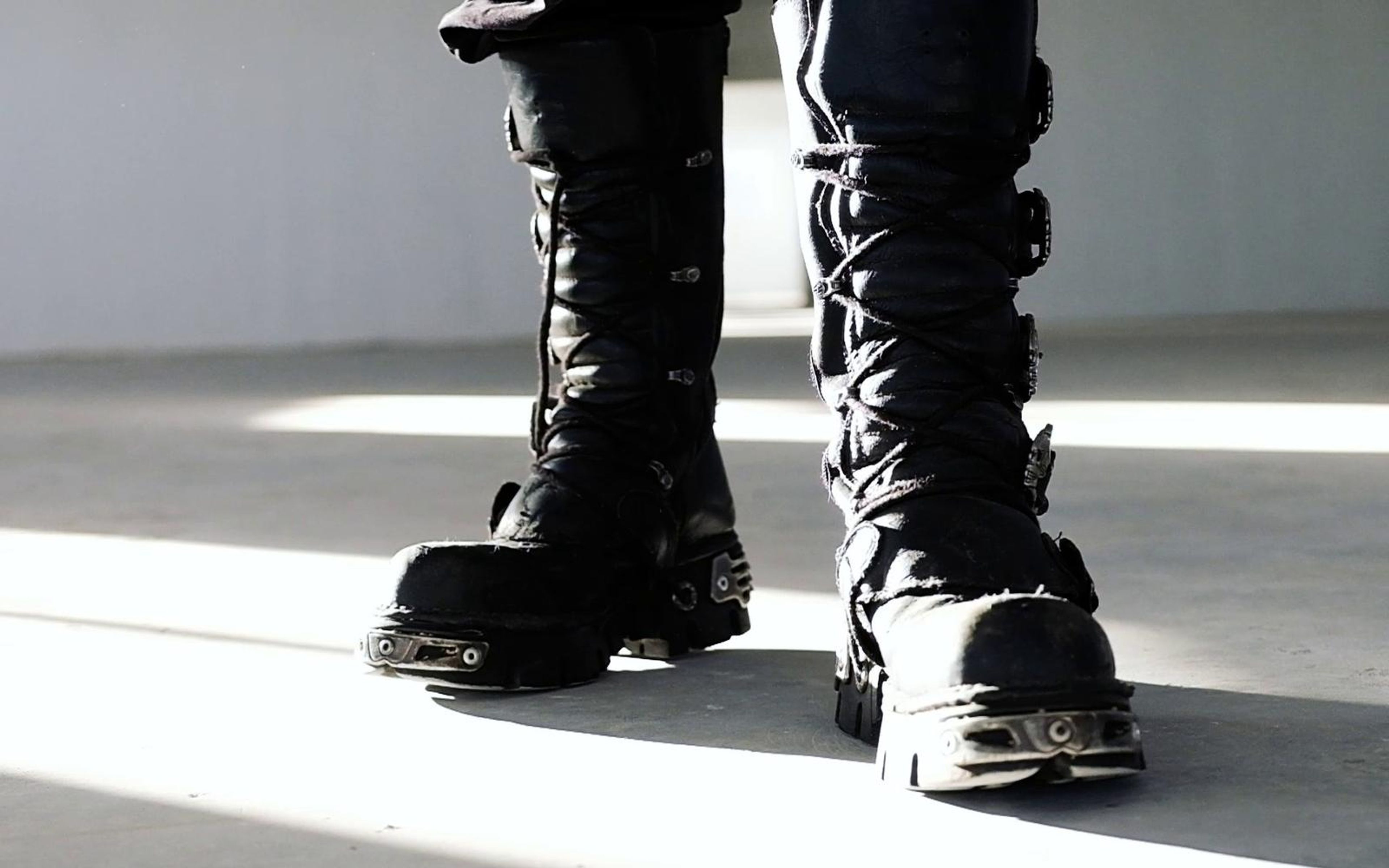Front view of two black buckled New Rock boots with metal toe caps standing in a streak of window light