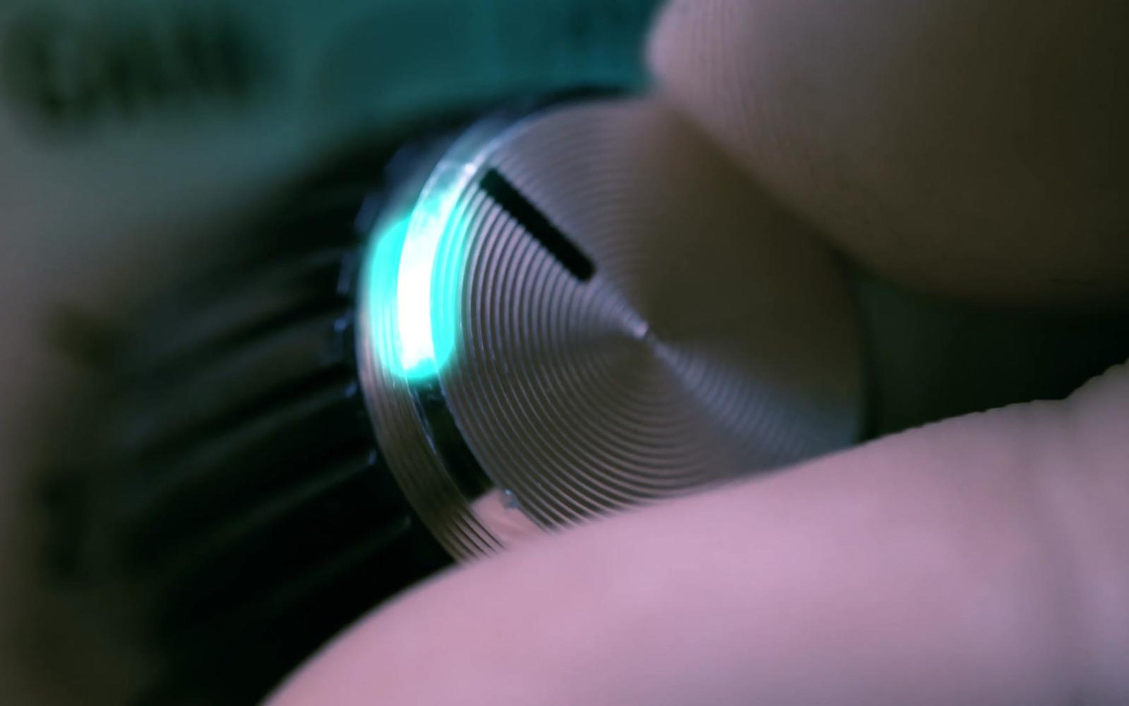 Close-up of a metal amp knob with a teal glow around its edge and a finger turning it