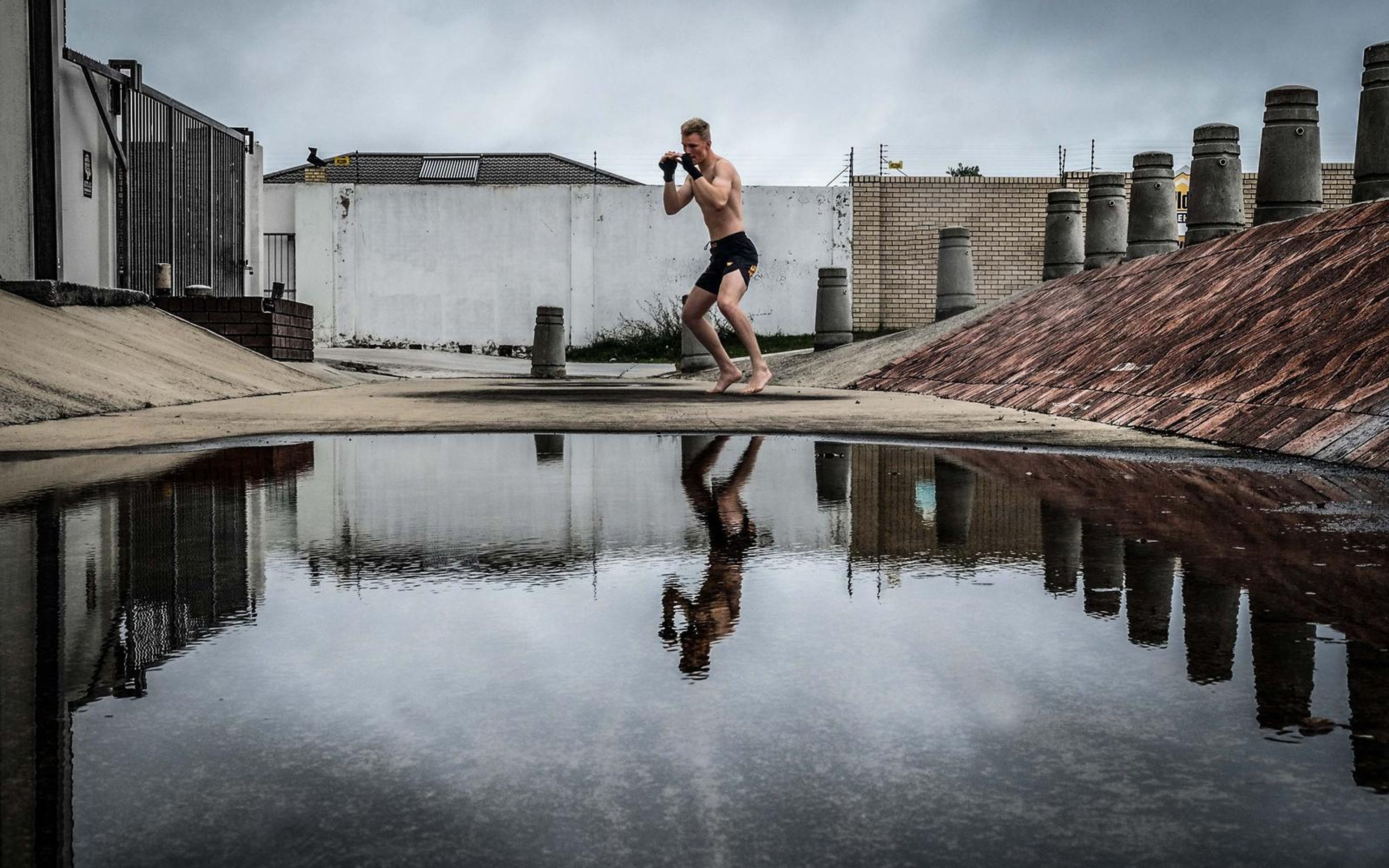 Man in a fighting stance beside a puddle, knees bent, reflection below him