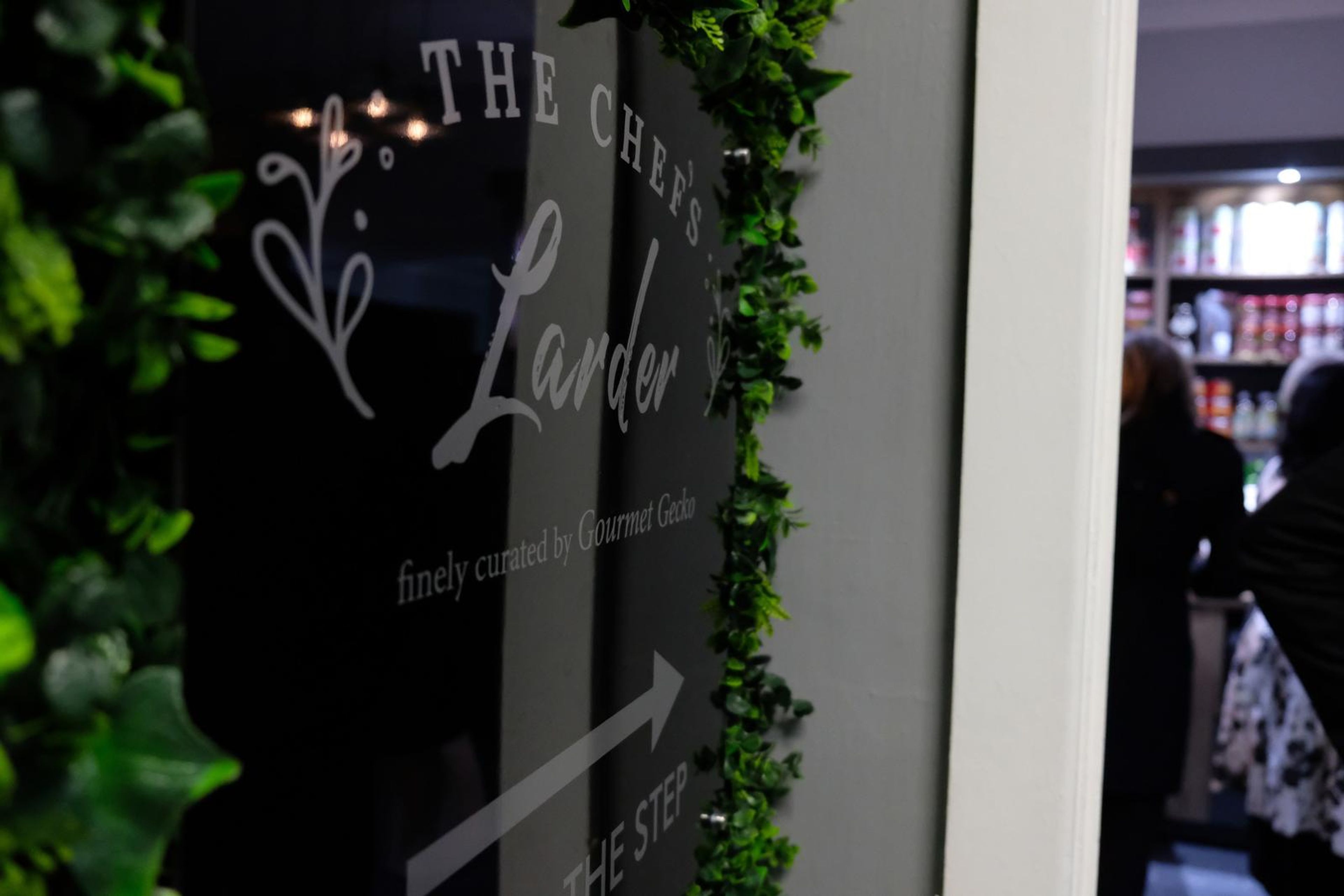 The Chef's Larder sign, finely curated by Gourmet Gecko, among green wall foliage