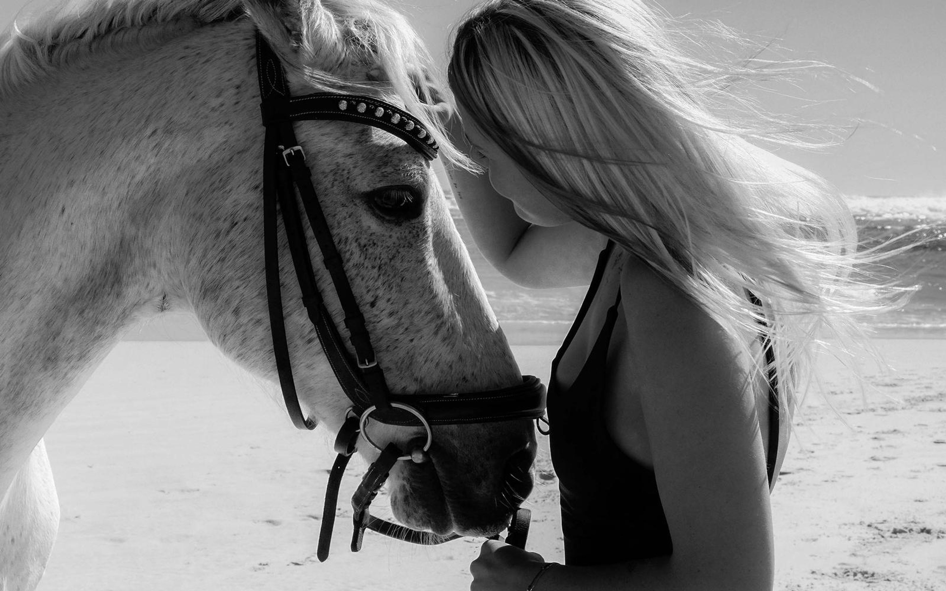 Black and white close view of a woman pressing her face to a horse's bridled head