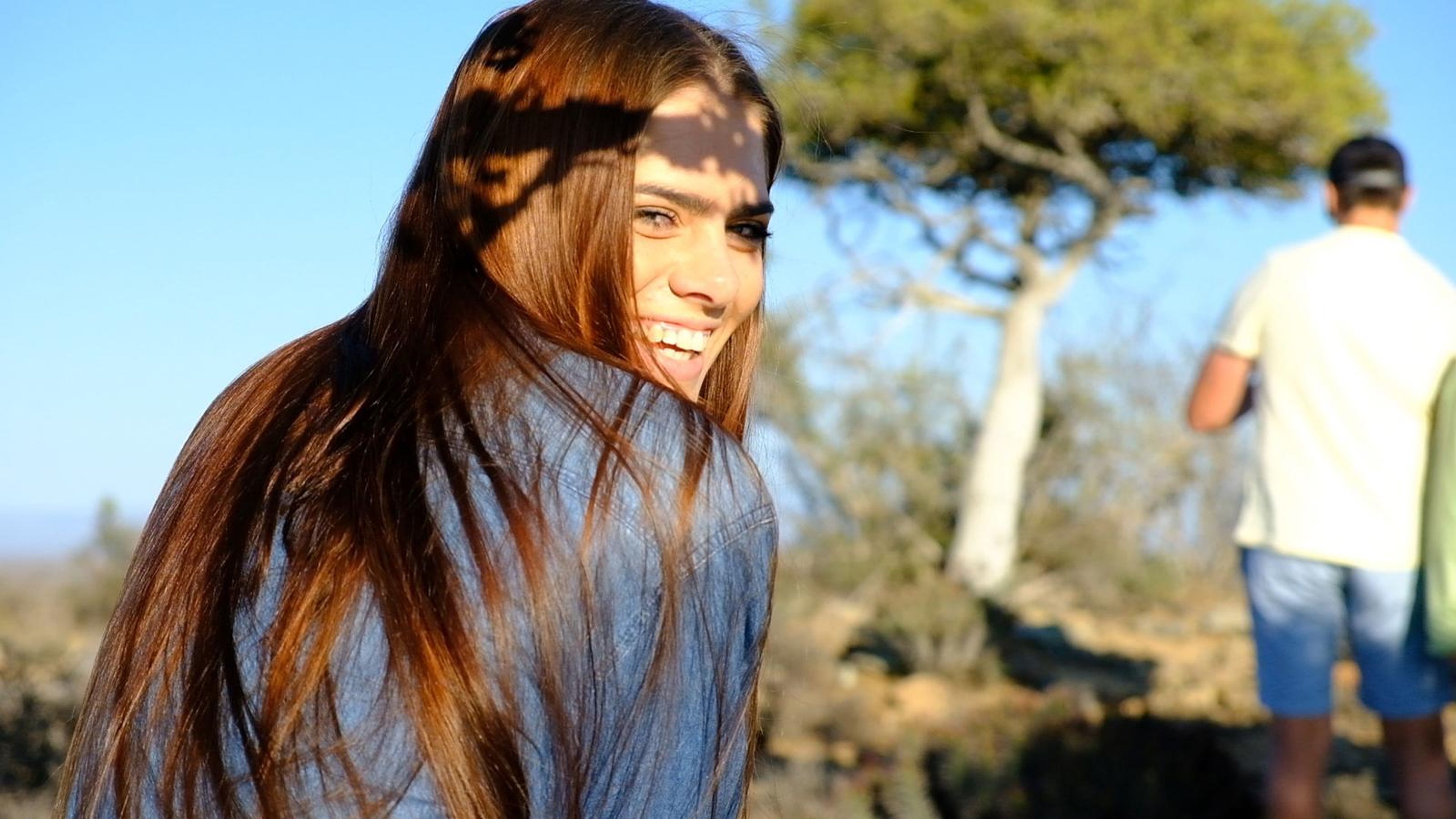 Model with long brown hair smiling over her shoulder
