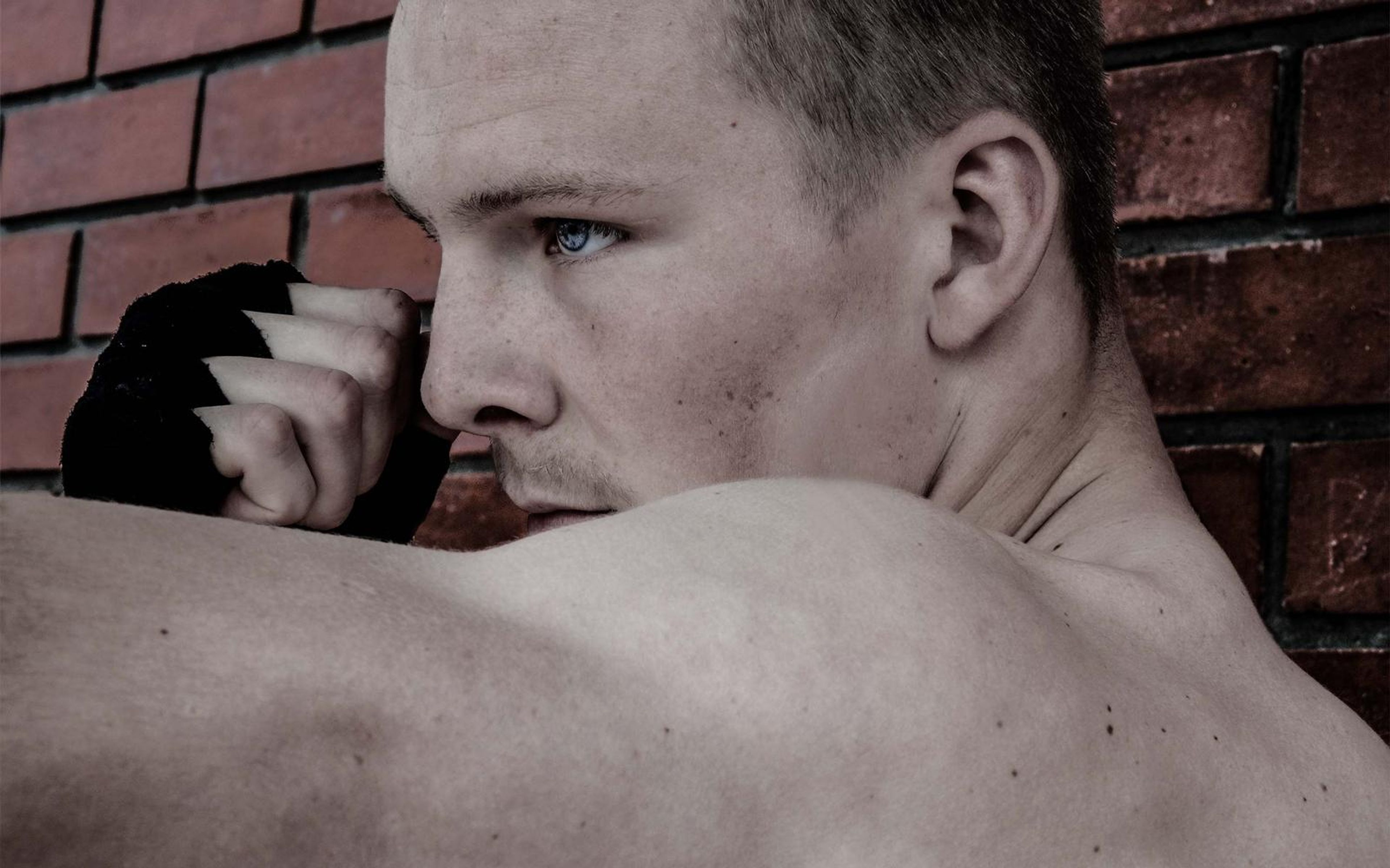 Side-on close-up of the fighter's face behind a wrapped fist with red brick behind