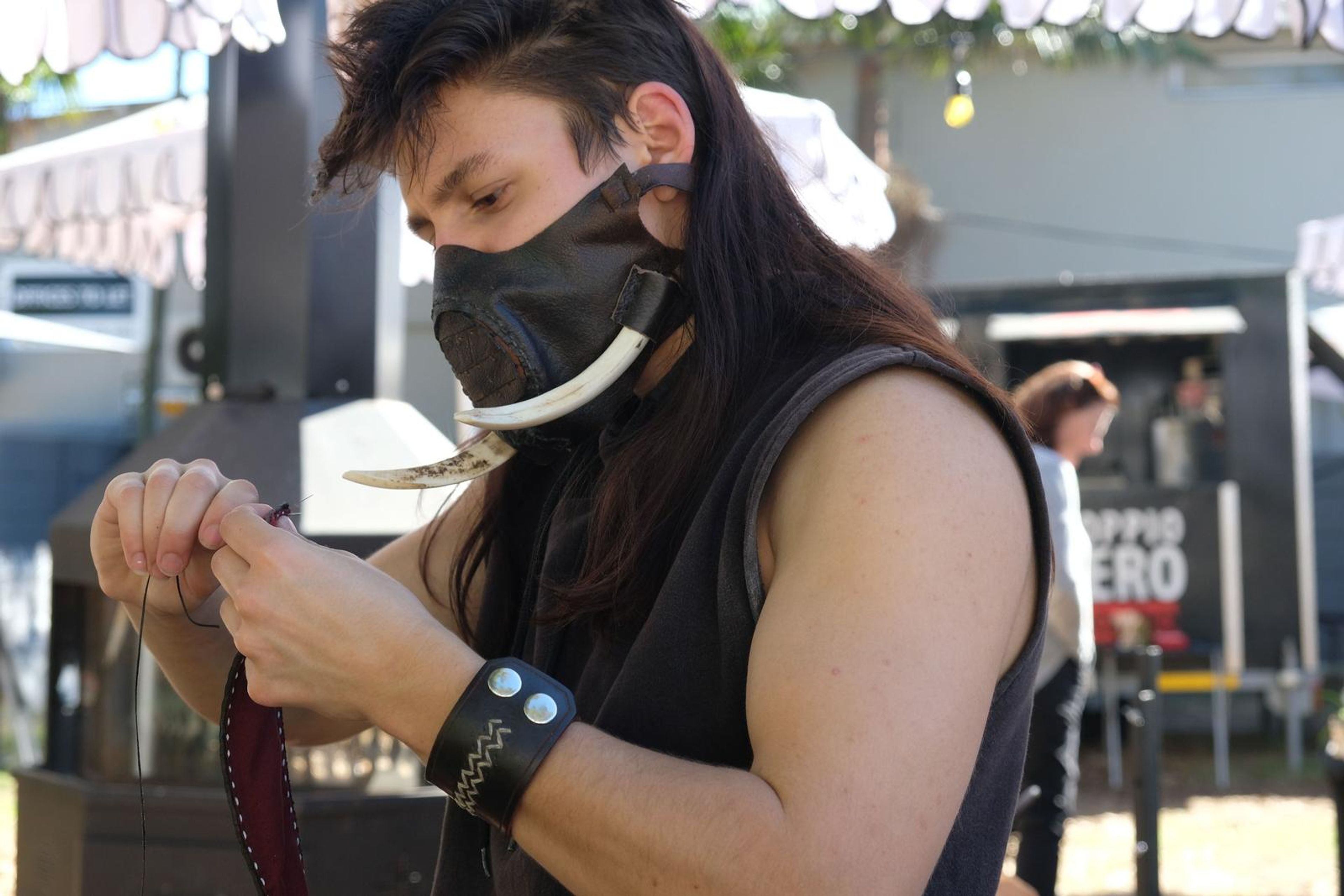 Close-up of the maker stitching a leather strap, wearing a handmade leather cuff