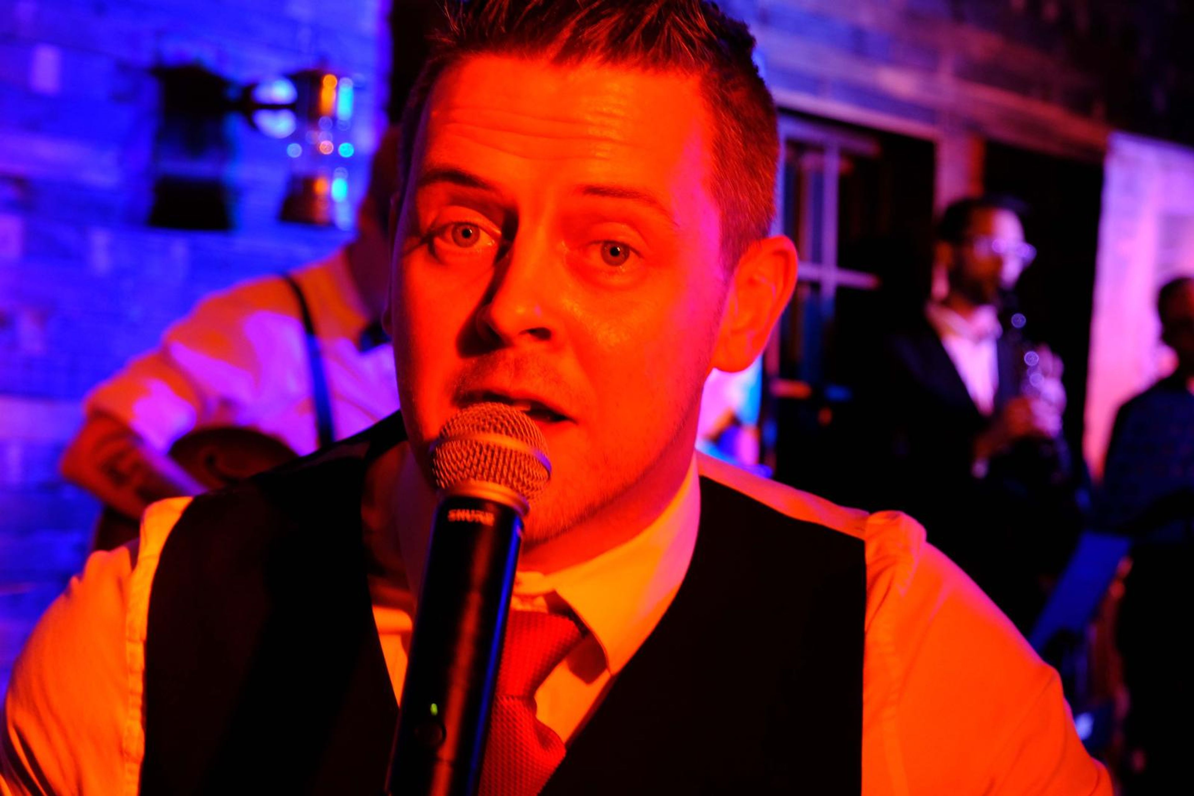 Close-up of a singer in a waistcoat singing into the microphone in orange light