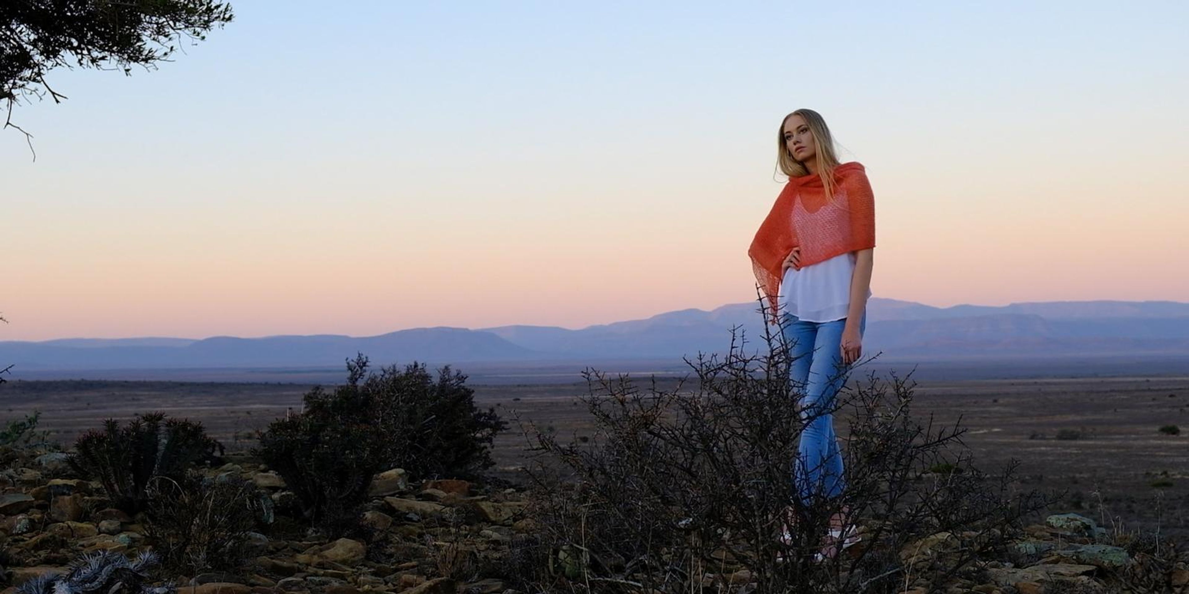 Model in a coral wrap standing on the veld at dusk