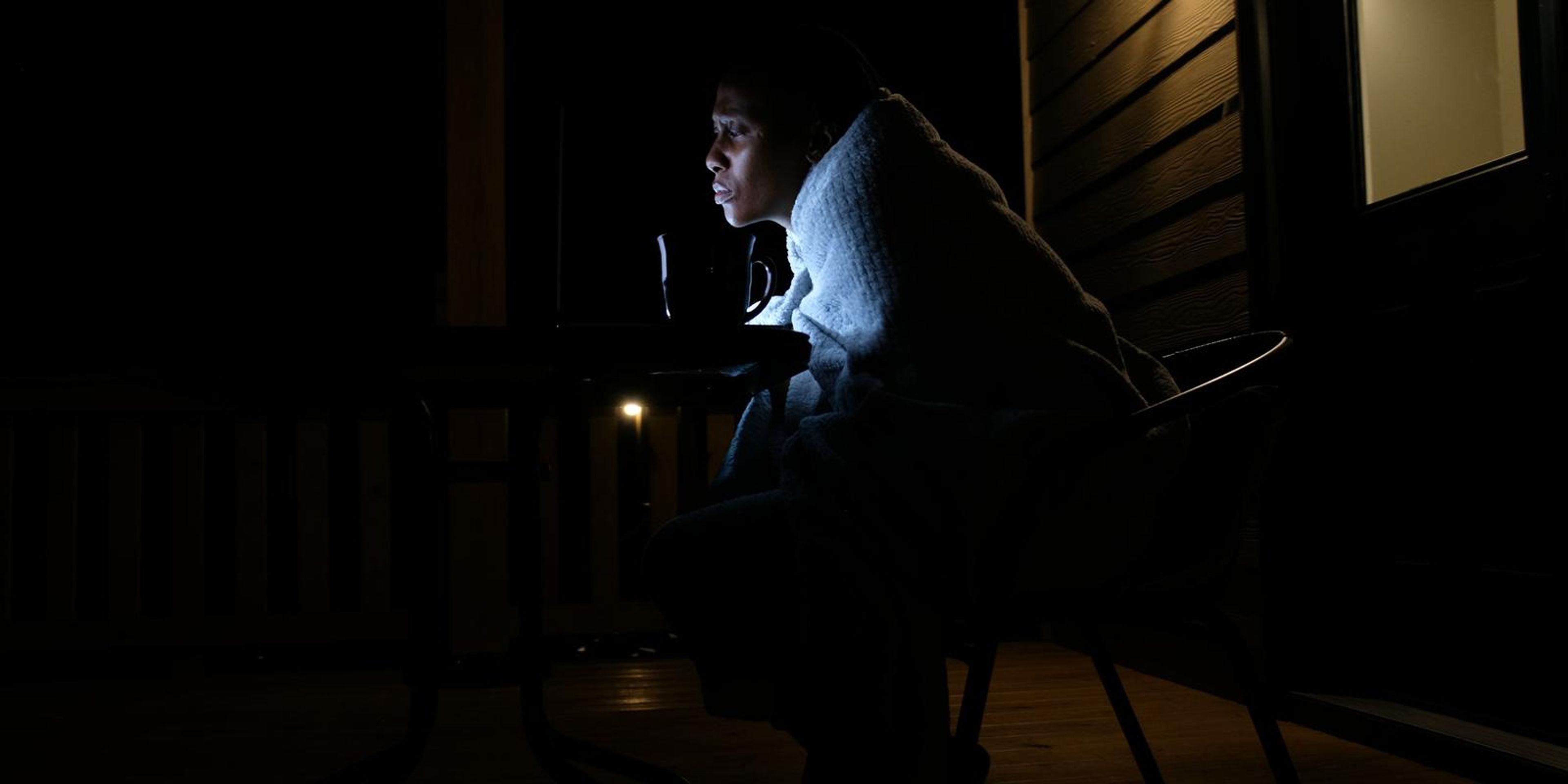 Frame of a woman lit only by her laptop screen on a dark porch at night