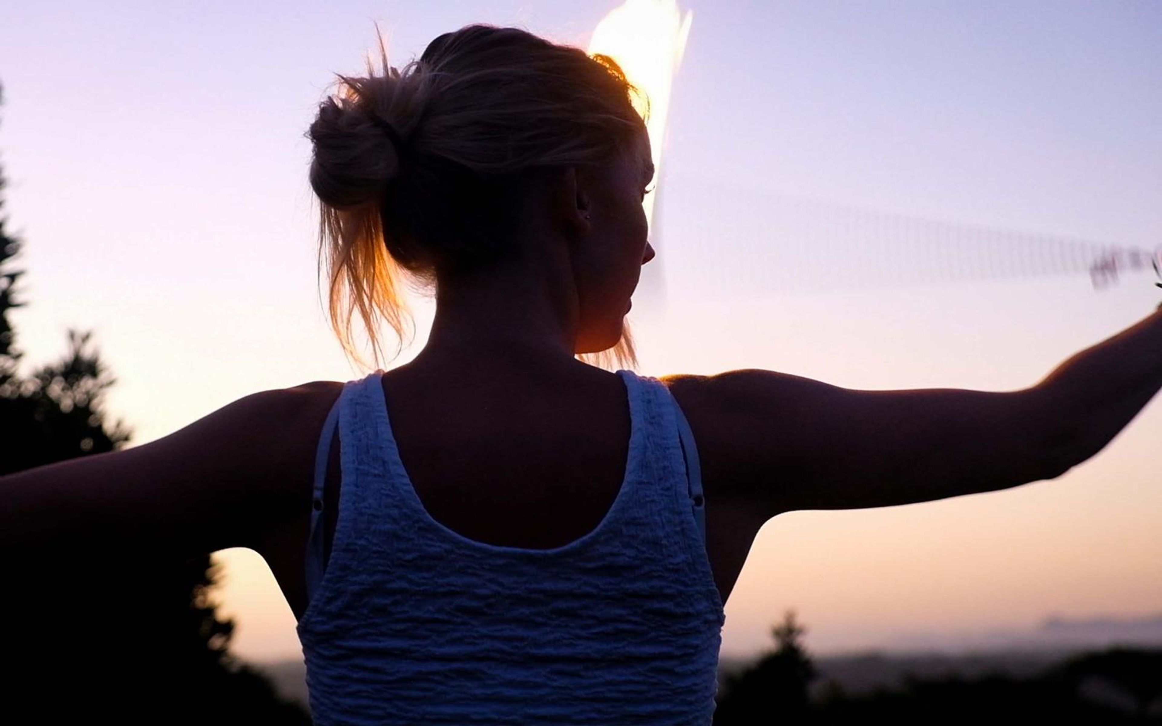 Woman seen from behind in a white top with arms stretched wide, a fire trail blurring at upper right