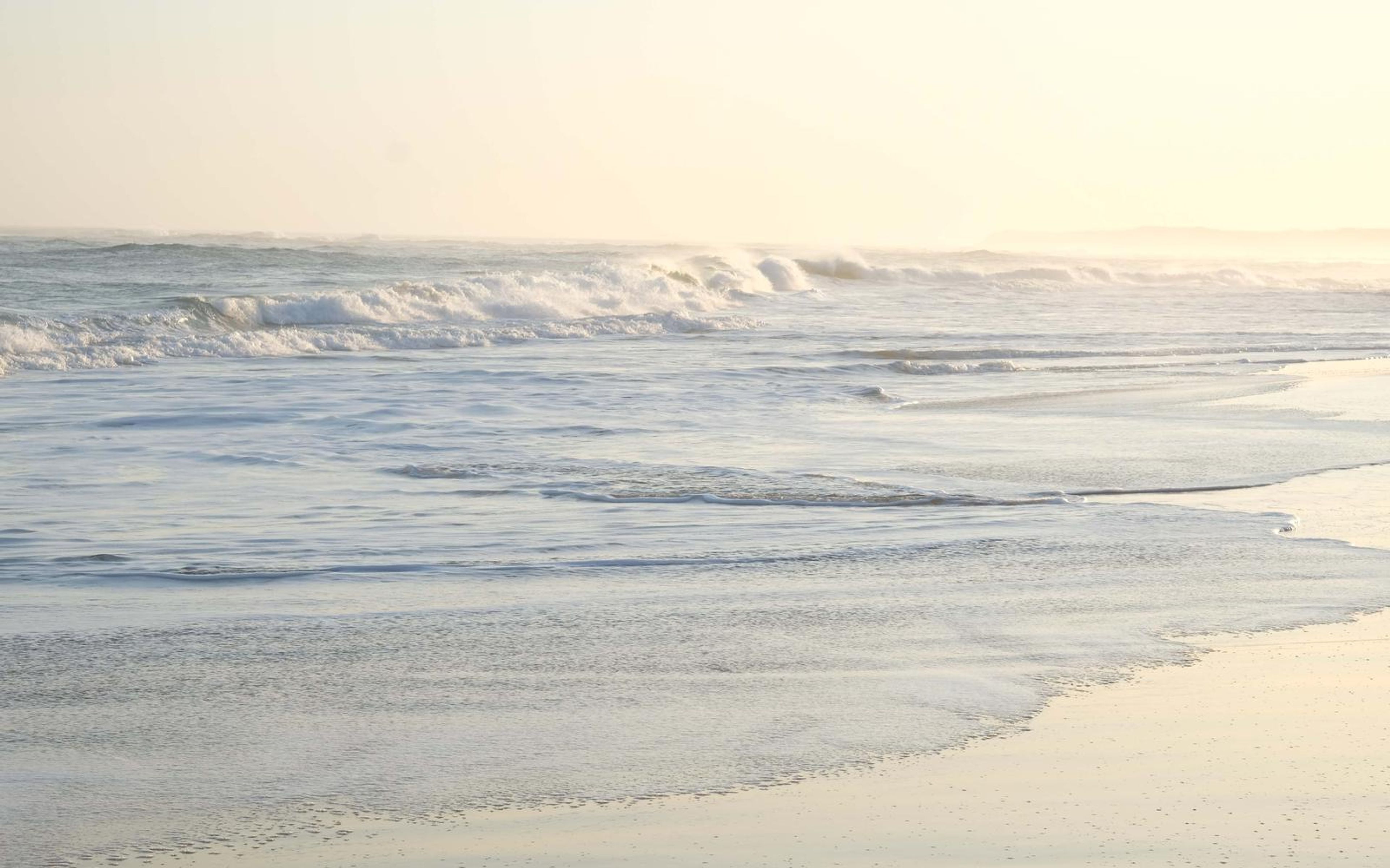 Golden light on foamy water sweeping up a gently sloping beach
