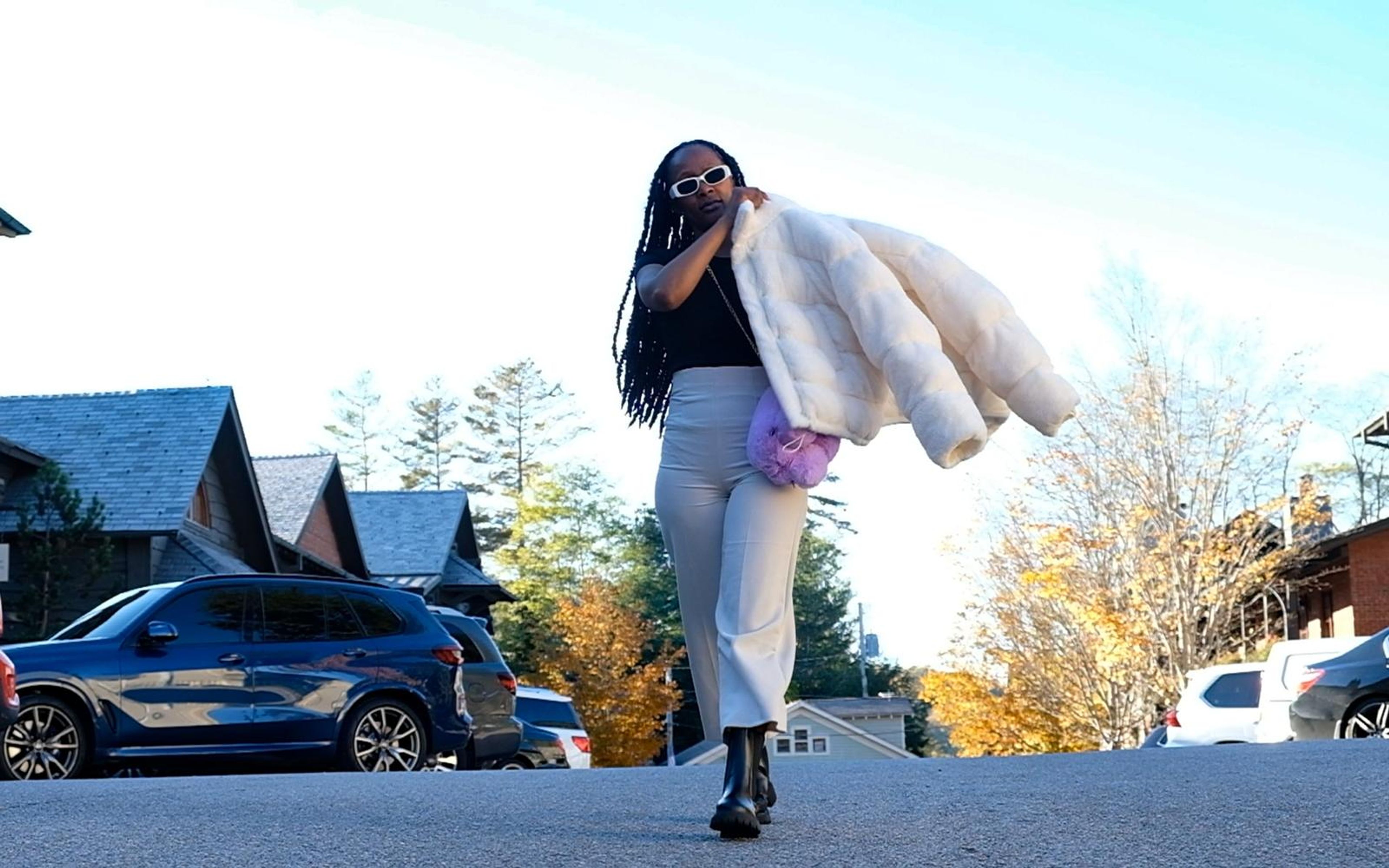 Model walking toward camera with the jacket slung over her shoulder, cream trousers, low angle