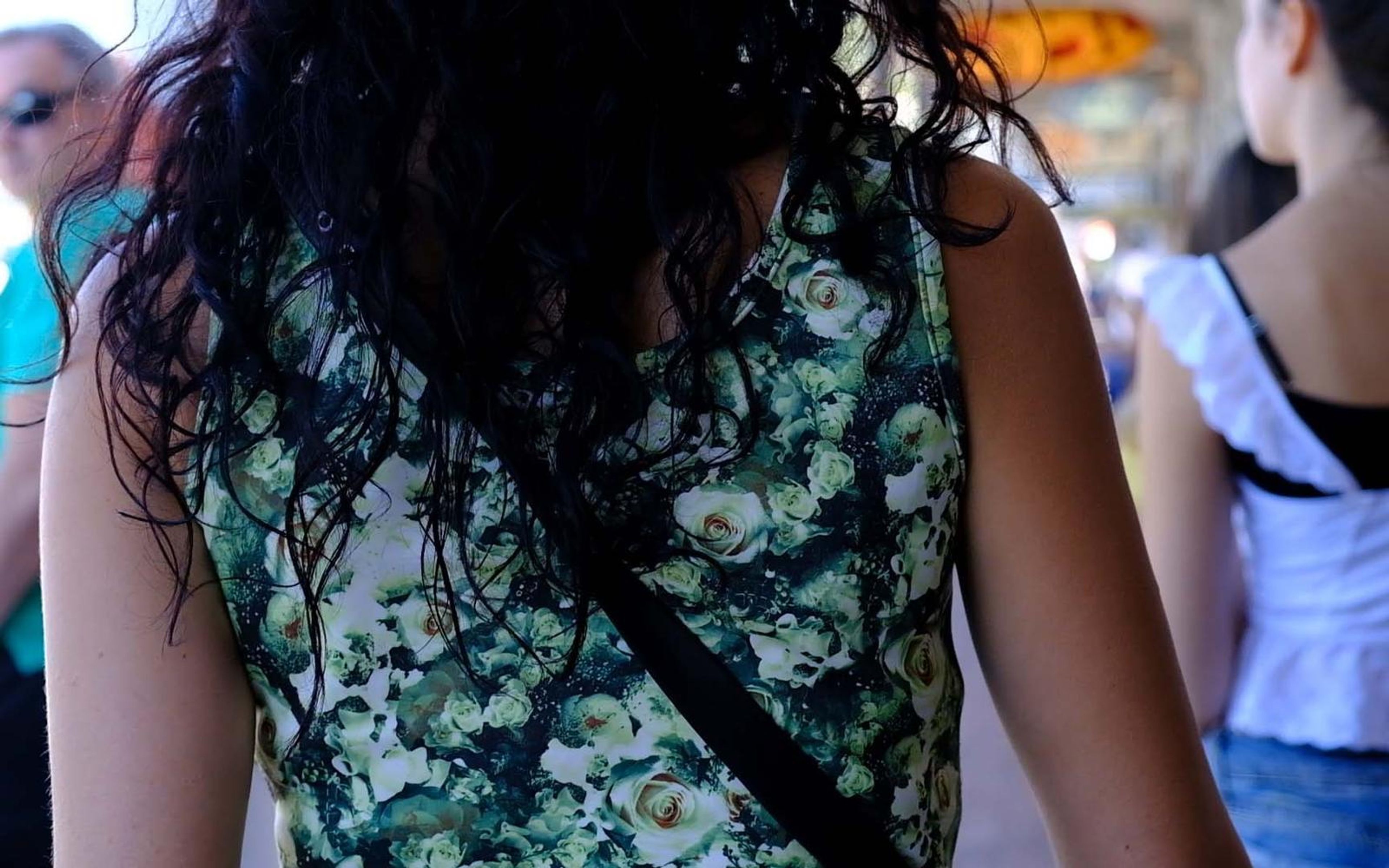 Woman in a green floral top with long dark curls seen from behind in a busy outdoor market