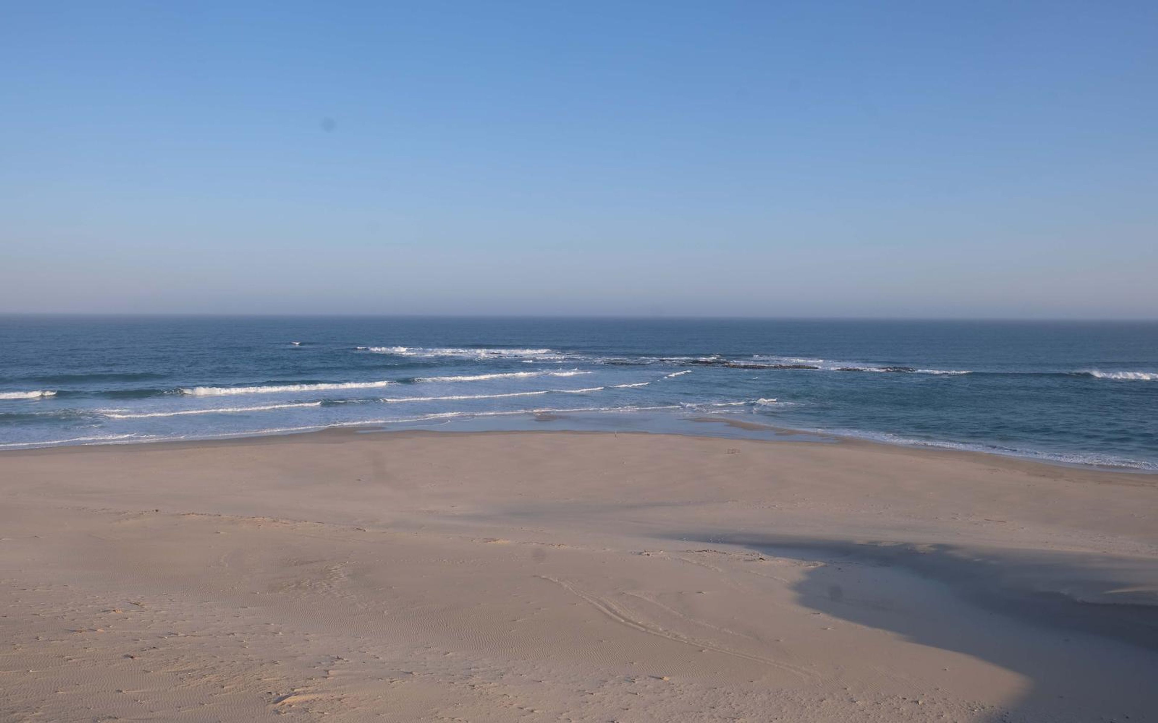 Empty beach and blue sea with white breaking waves under a clear sky