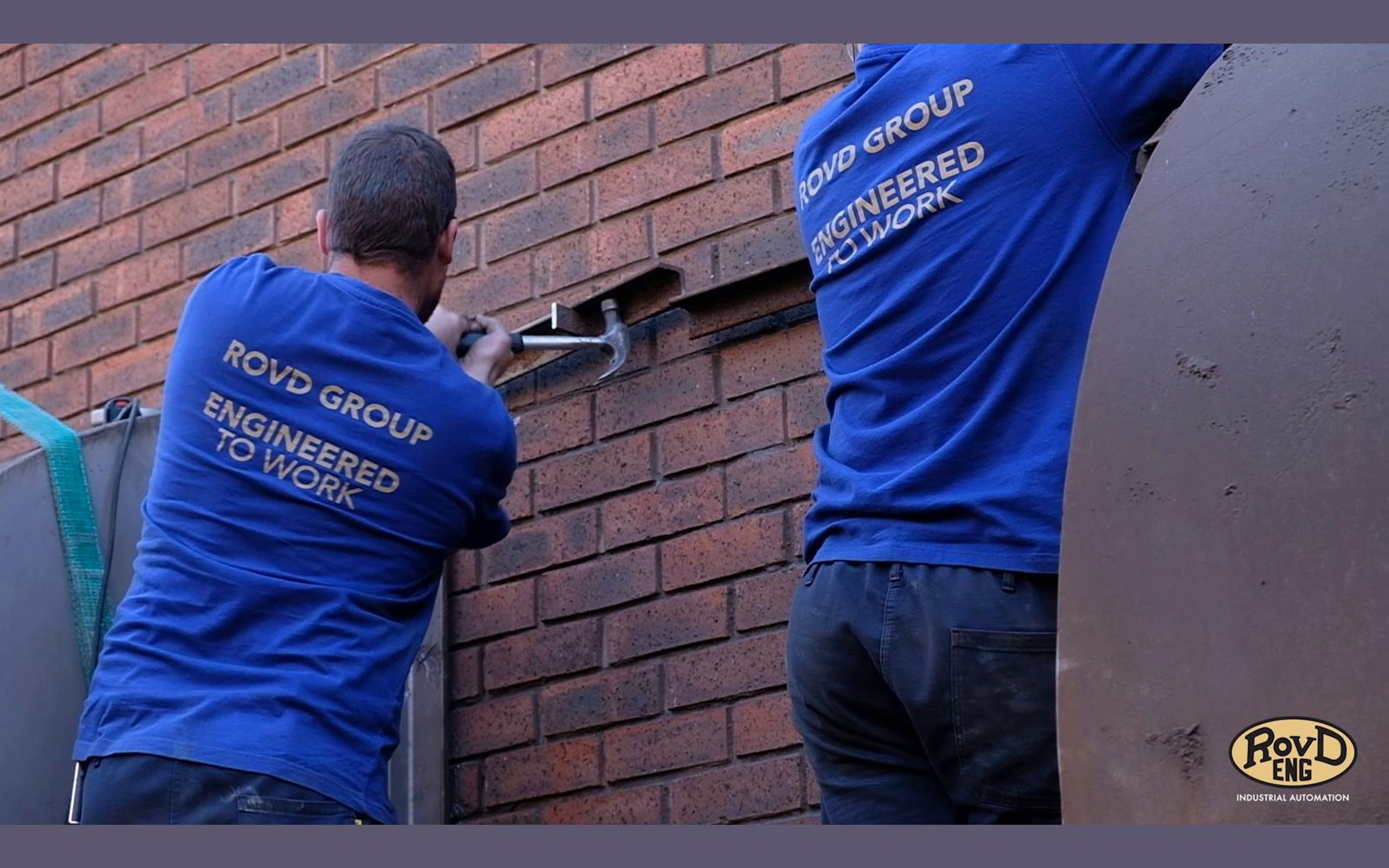 Workers fitting a steel panel to a brick wall
