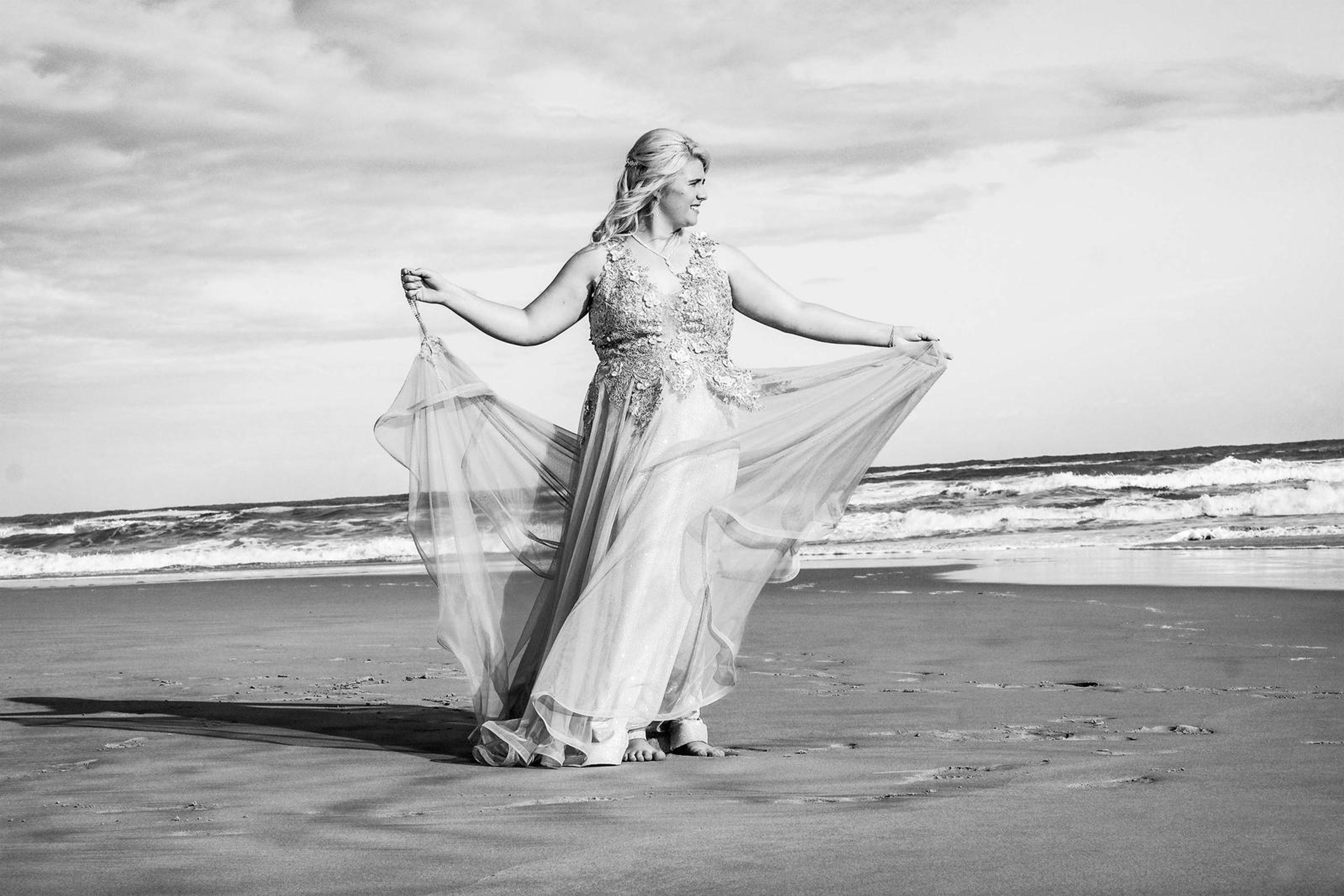 Black and white portrait holding out the gown on both sides beside the waves