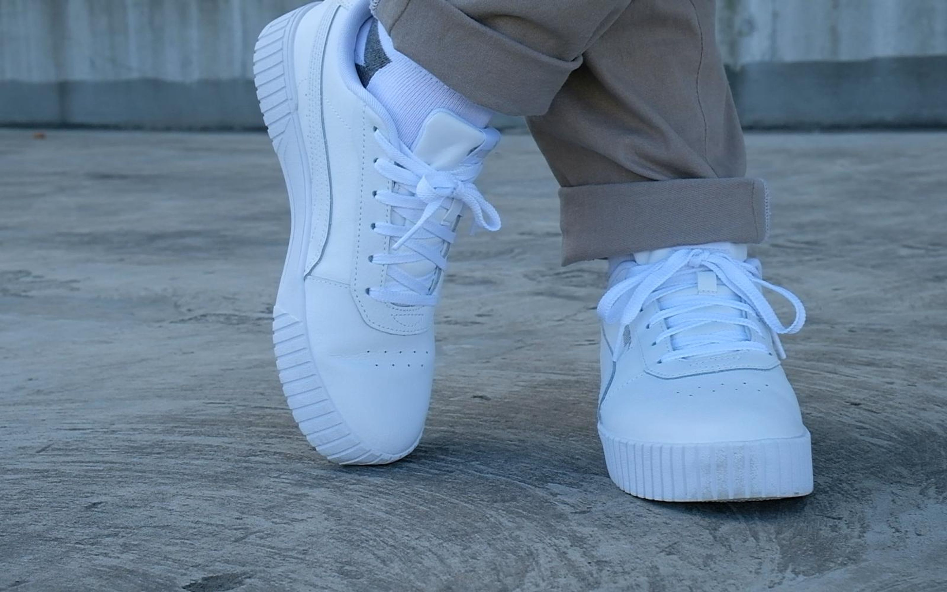 White sneakers crossed at the ankles on a concrete floor, laces and chunky white soles in focus