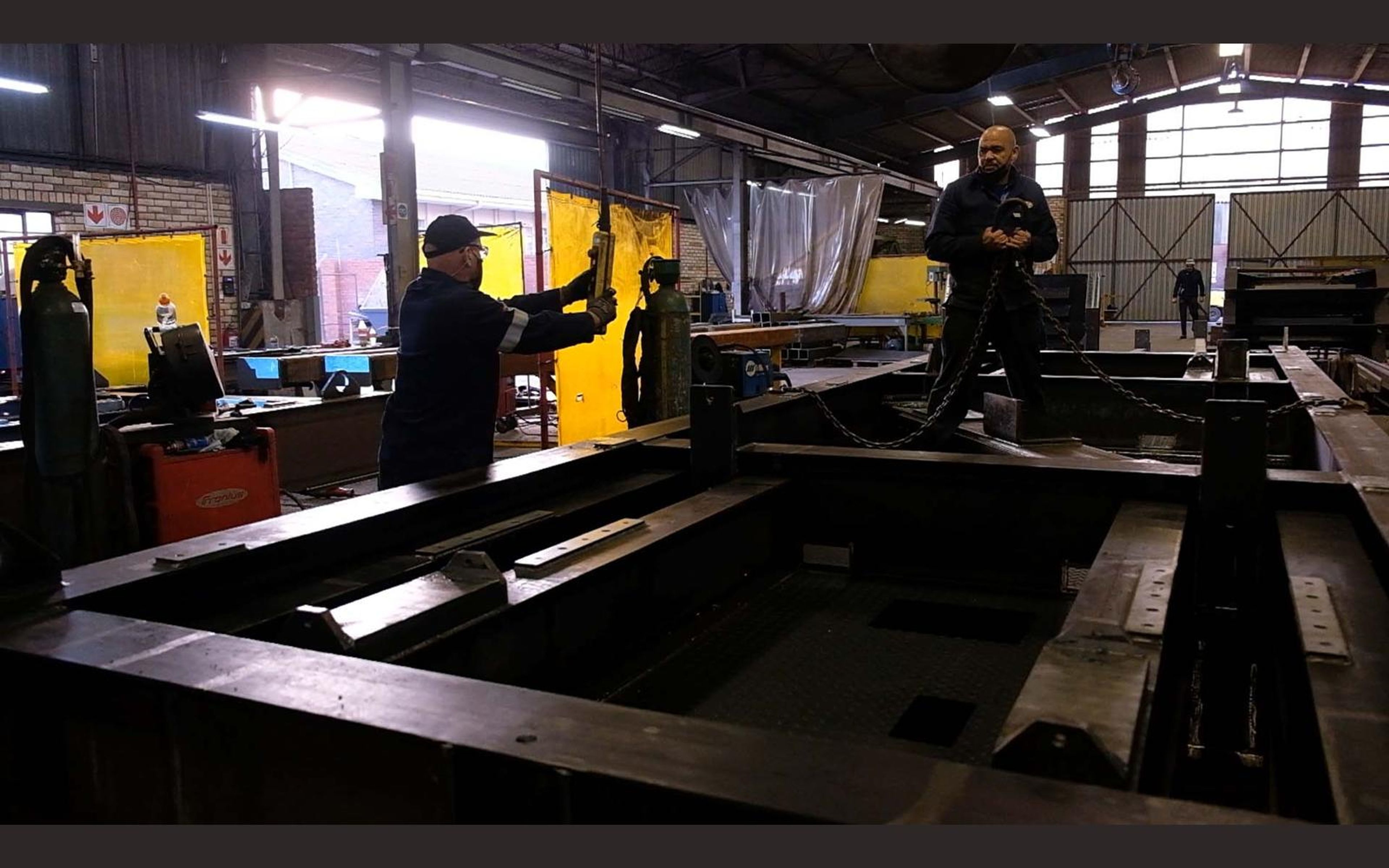 Fabricators at work among steel beams in the shop