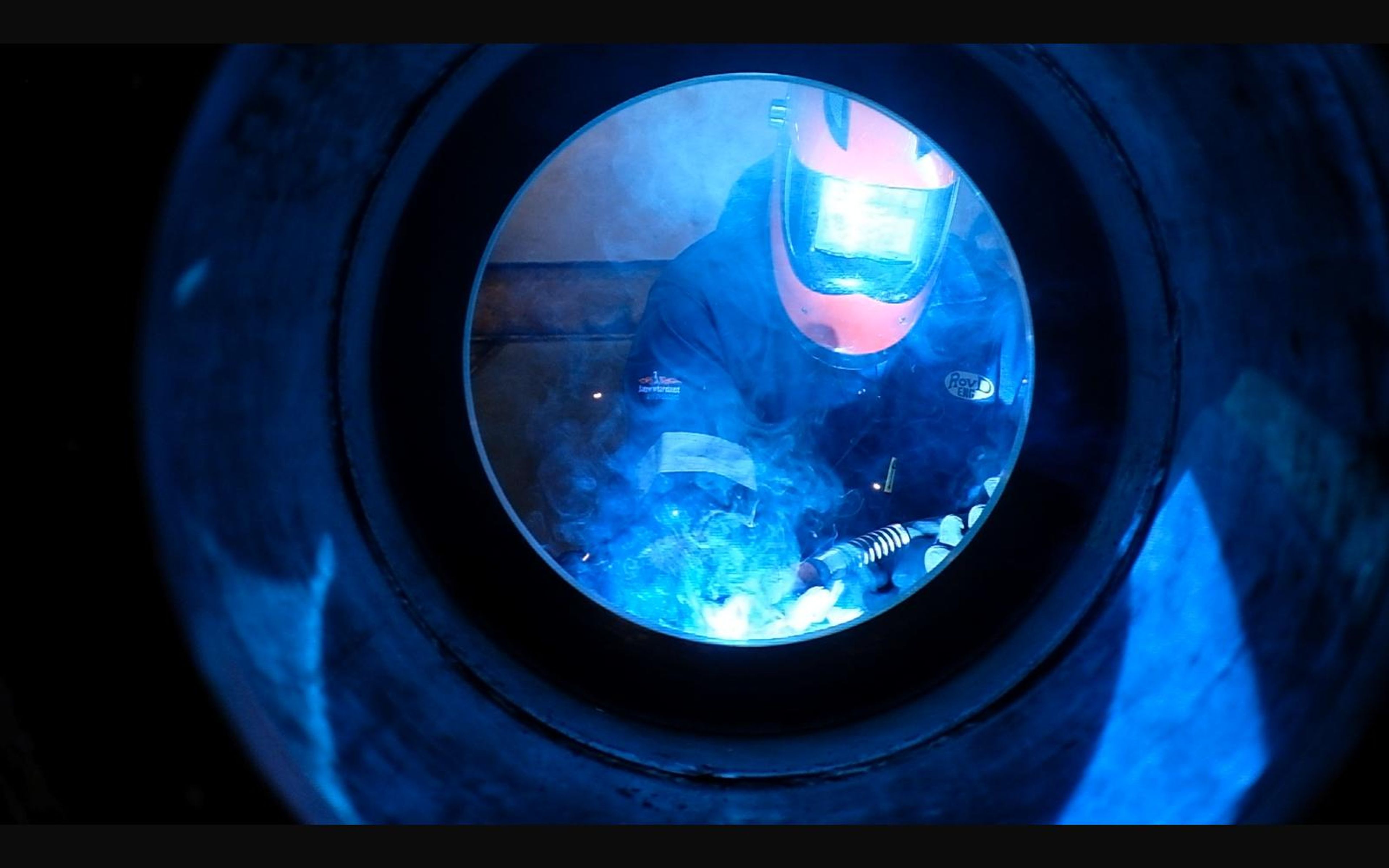 Welder seen through a round steel opening