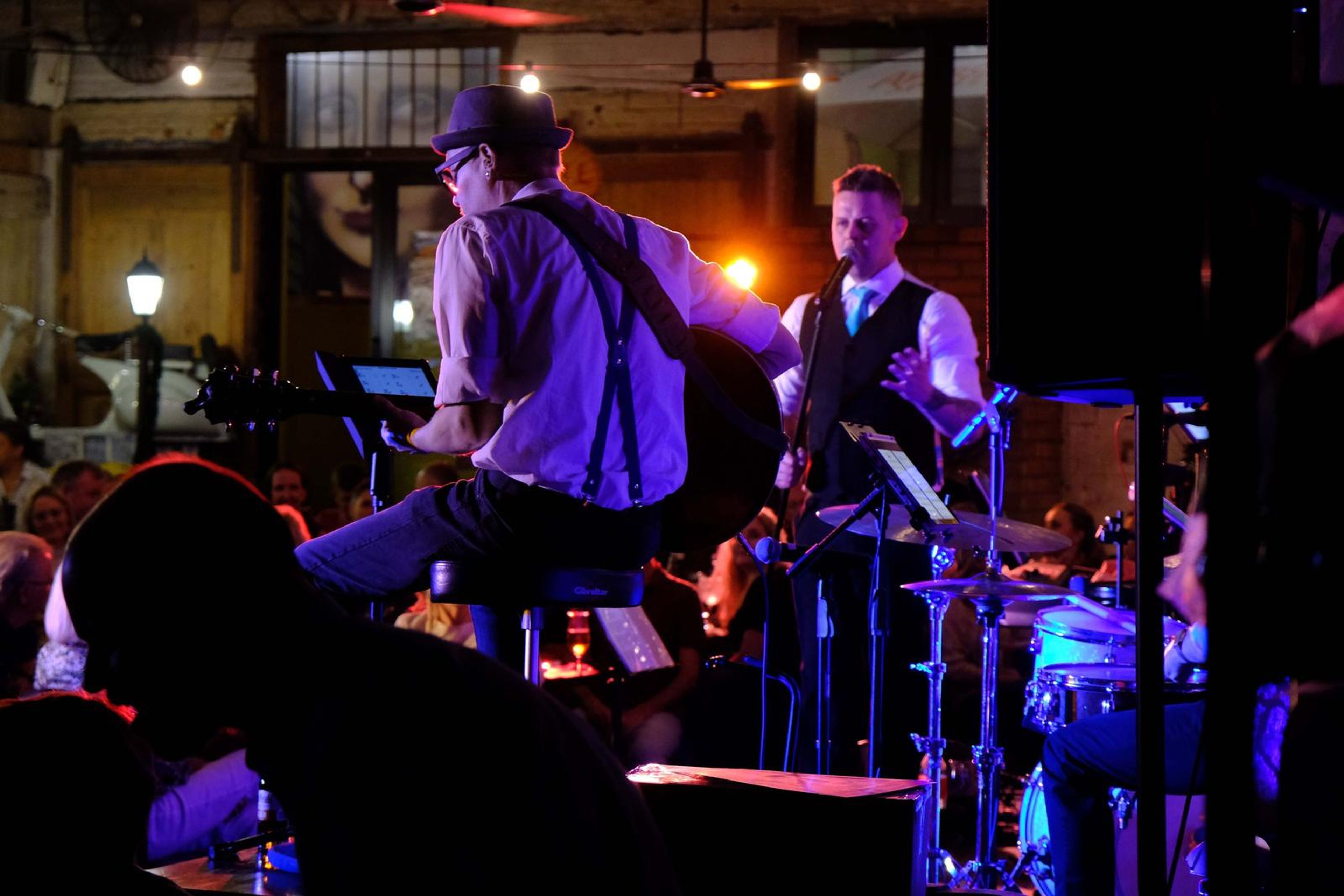 Guitarist in a hat and suspenders playing while a singer joins him
