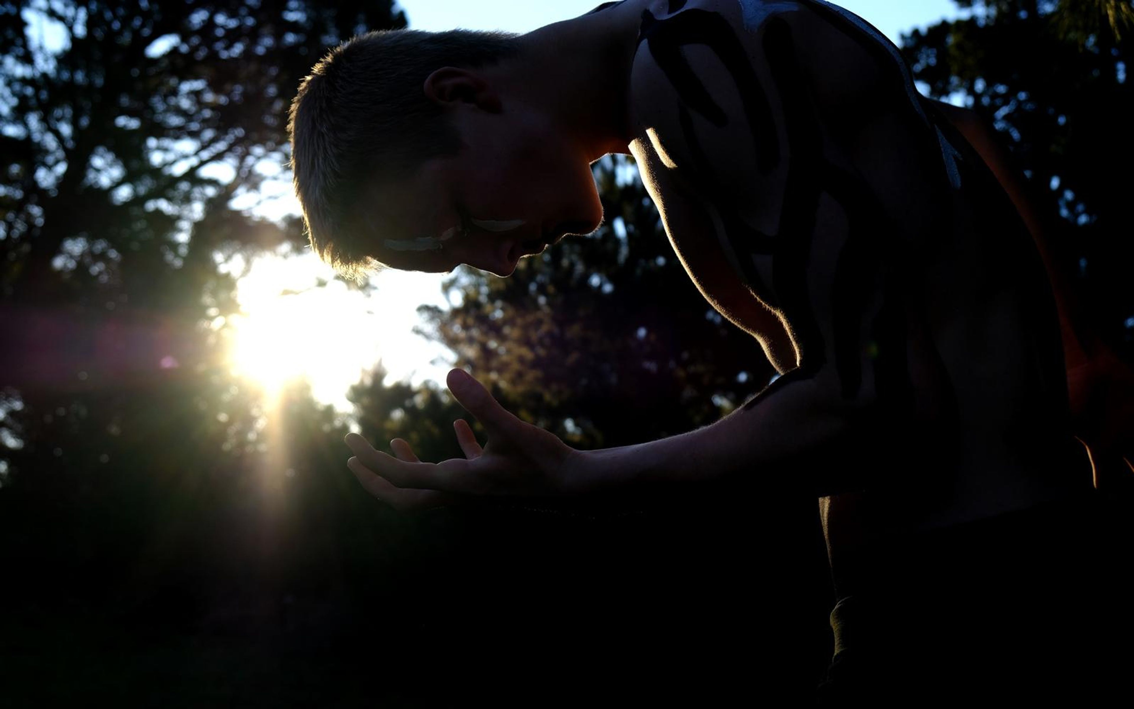Silhouette of the performer bowing his head toward the low sun with rim light around his shoulders