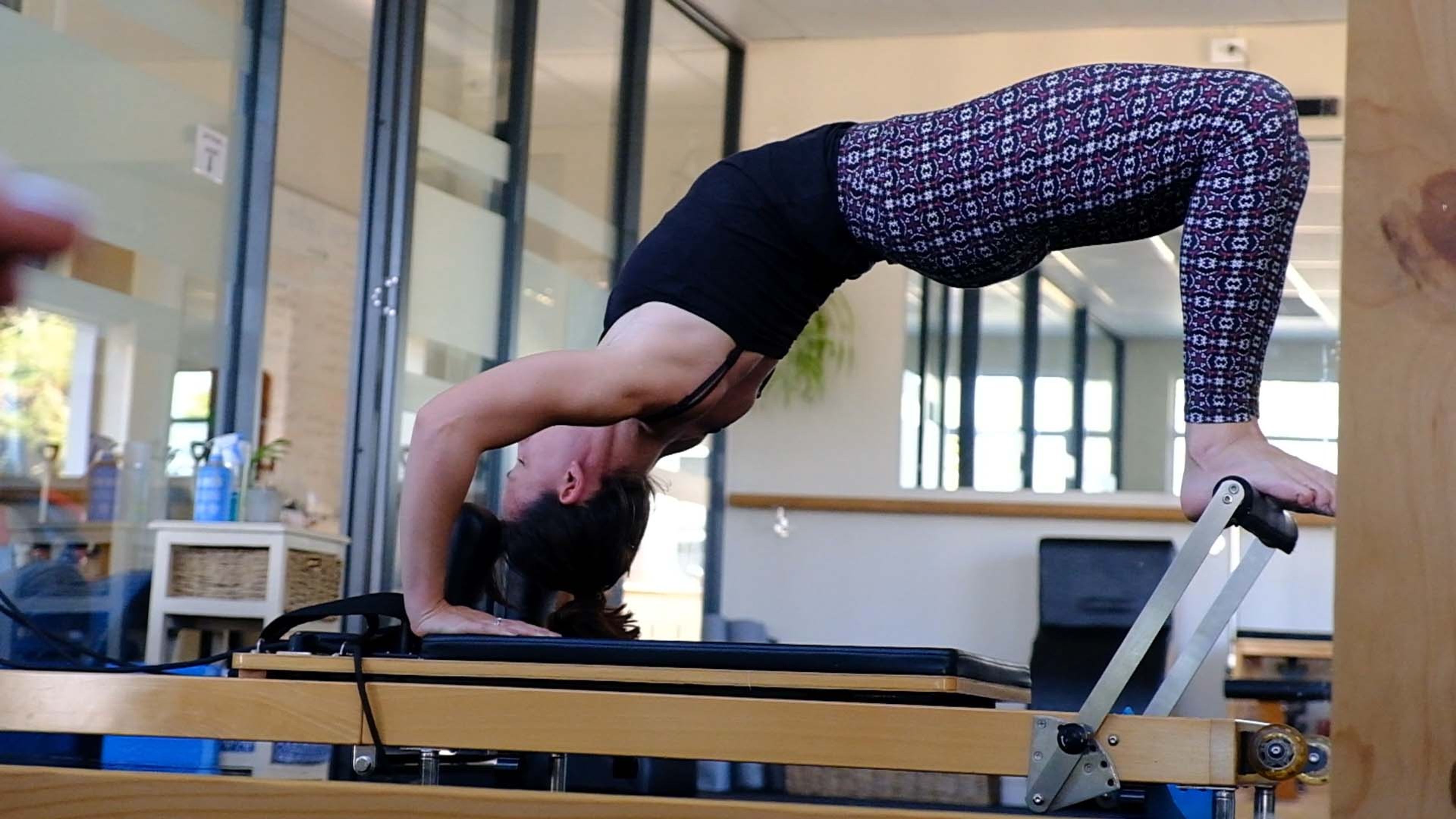 Woman in a back-arch on a Pilates reformer, wide view
