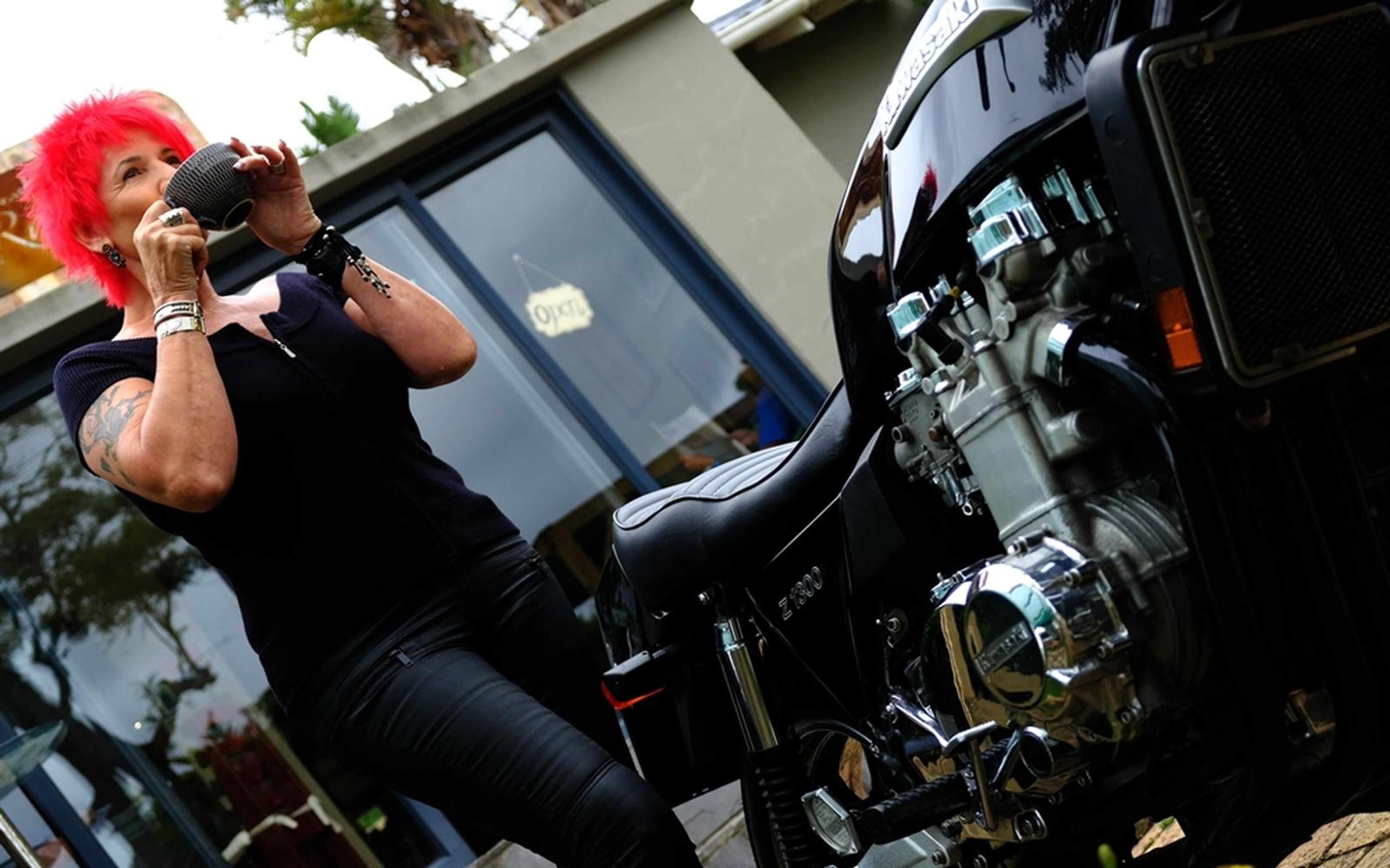 Woman with red hair leaning on a motorbike, sipping from a cup, low tilted angle