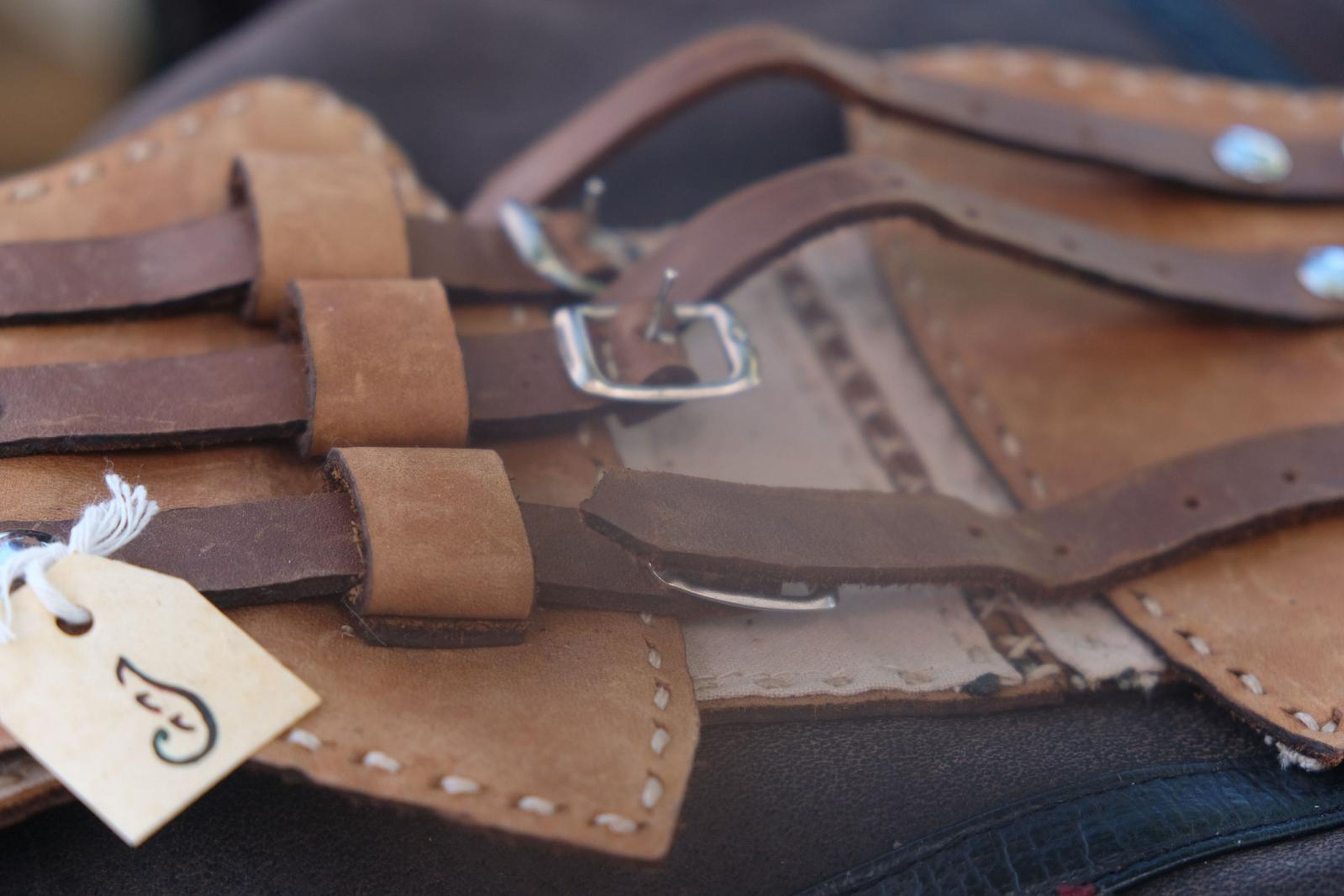 Close-up of tan and brown buckled leather straps with a handwritten tag