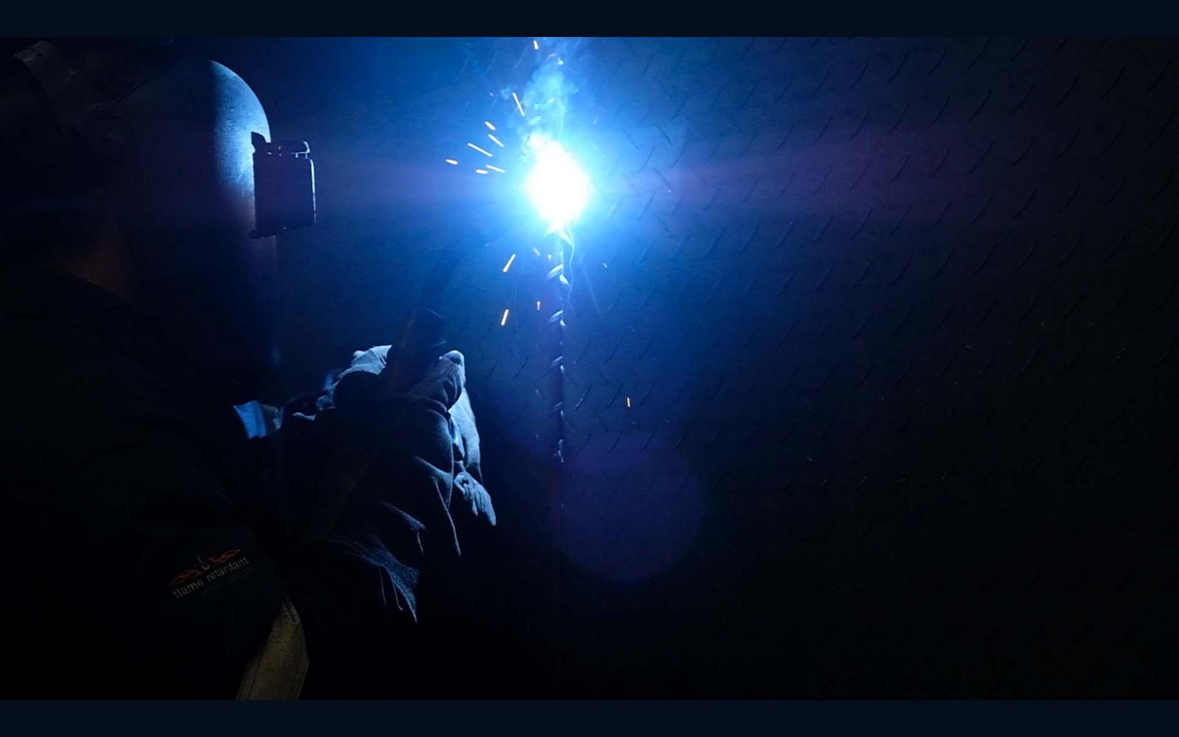 Distant welder lit only by the weld arc