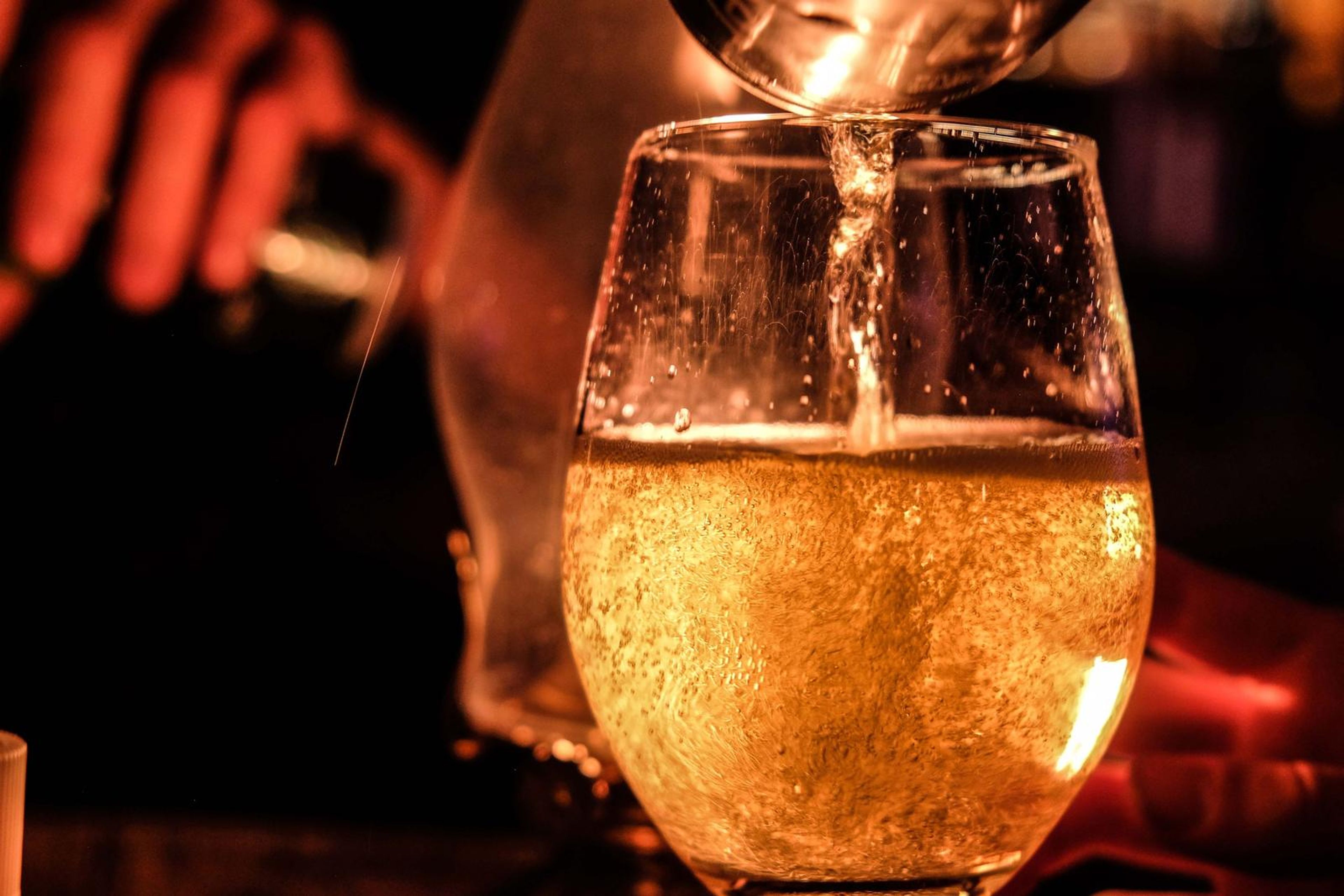 Glass of white wine being poured, glowing in the bar light