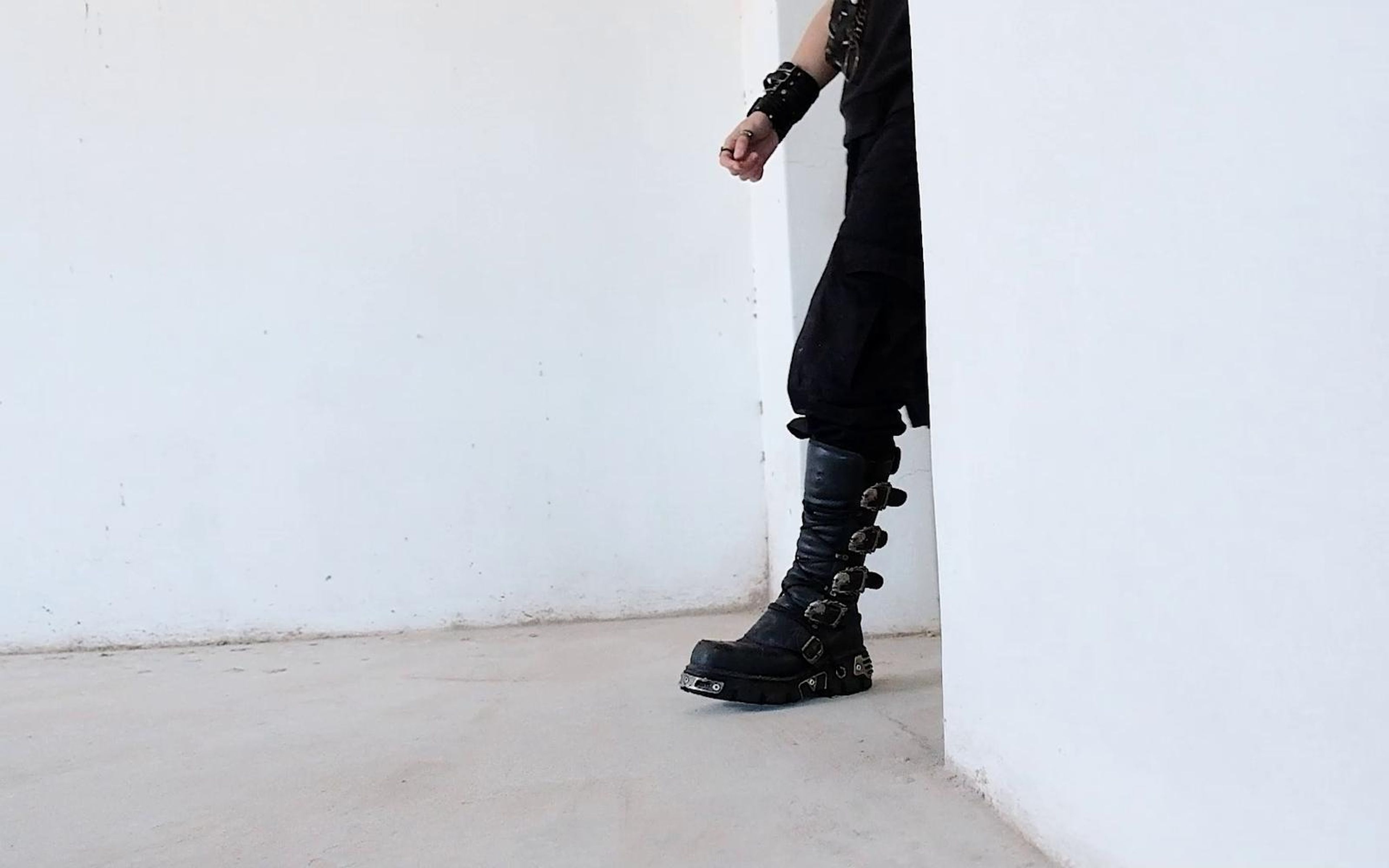 Tall buckled New Rock boot and a clenched hand by a white wall edge, shot from low and close