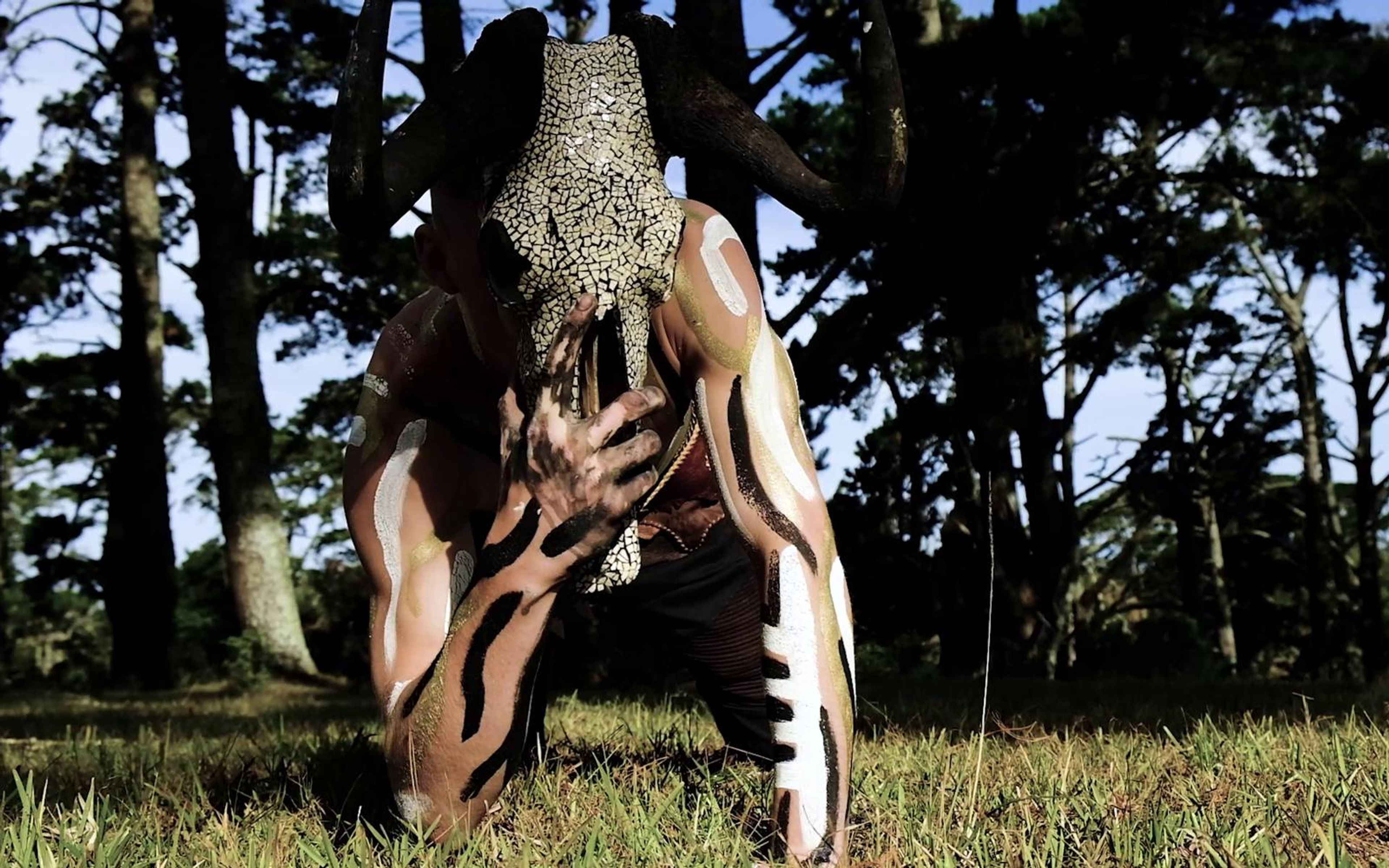 Figure crouching on grass in the distance with a skull mask on his head
