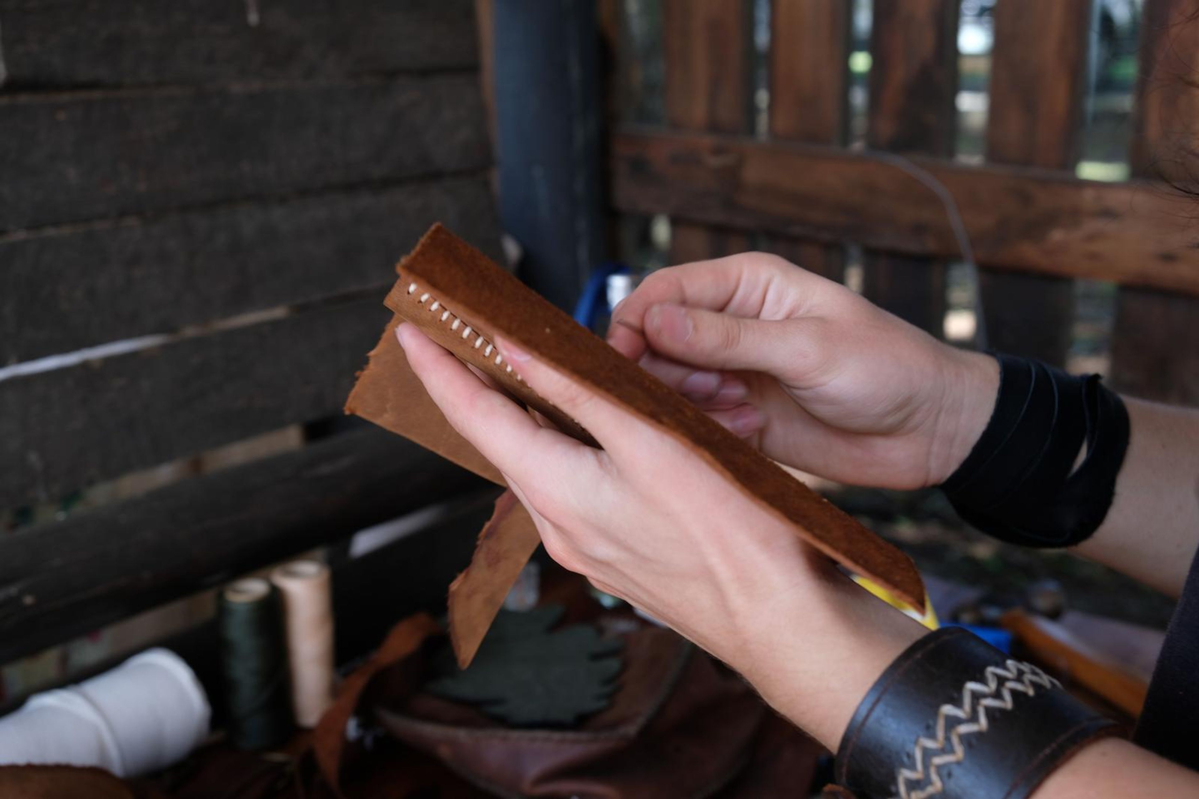 Hands lacing a small piece of tan leather with waxed thread