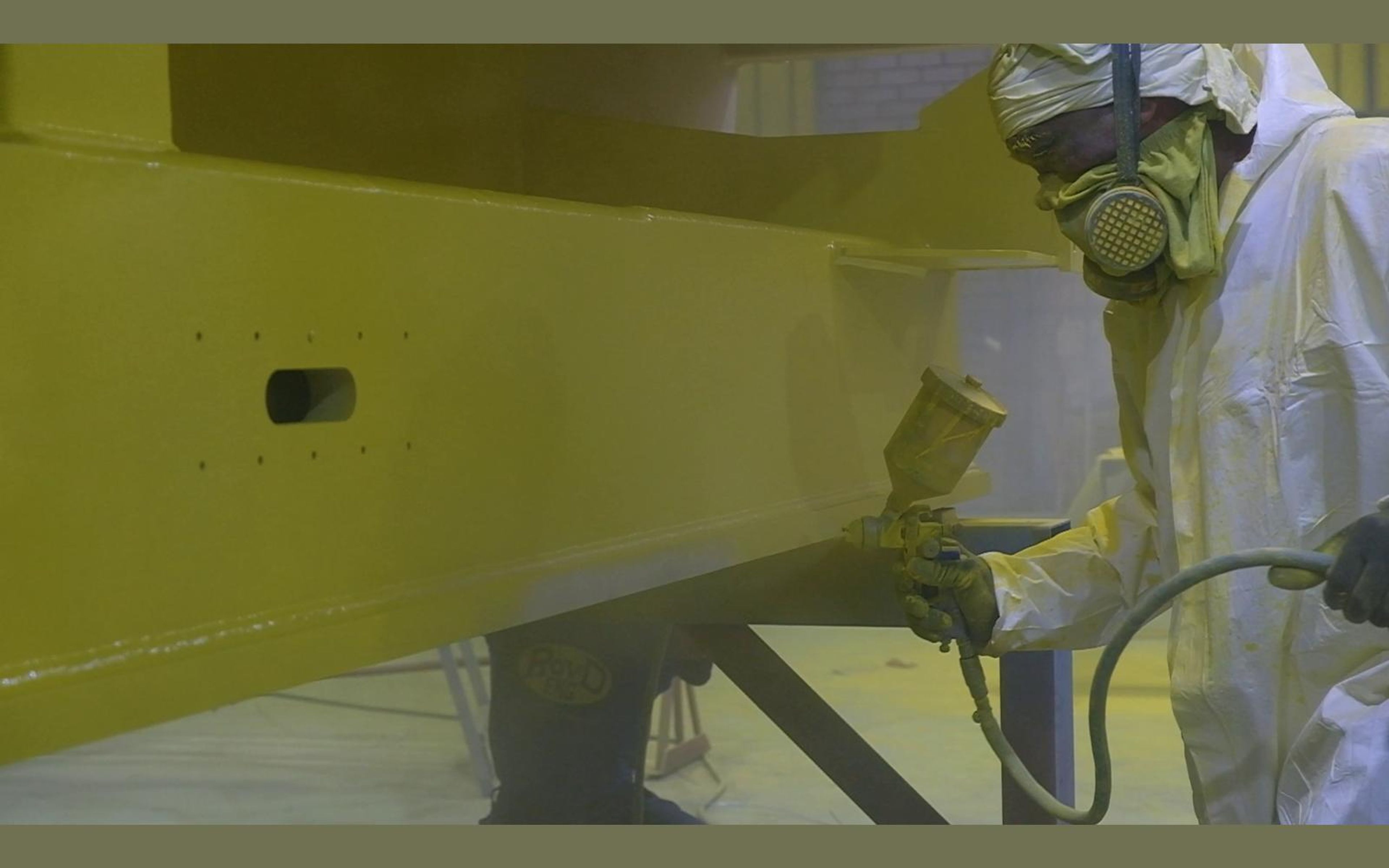 Painter spraying a yellow beam with a respirator and white suit