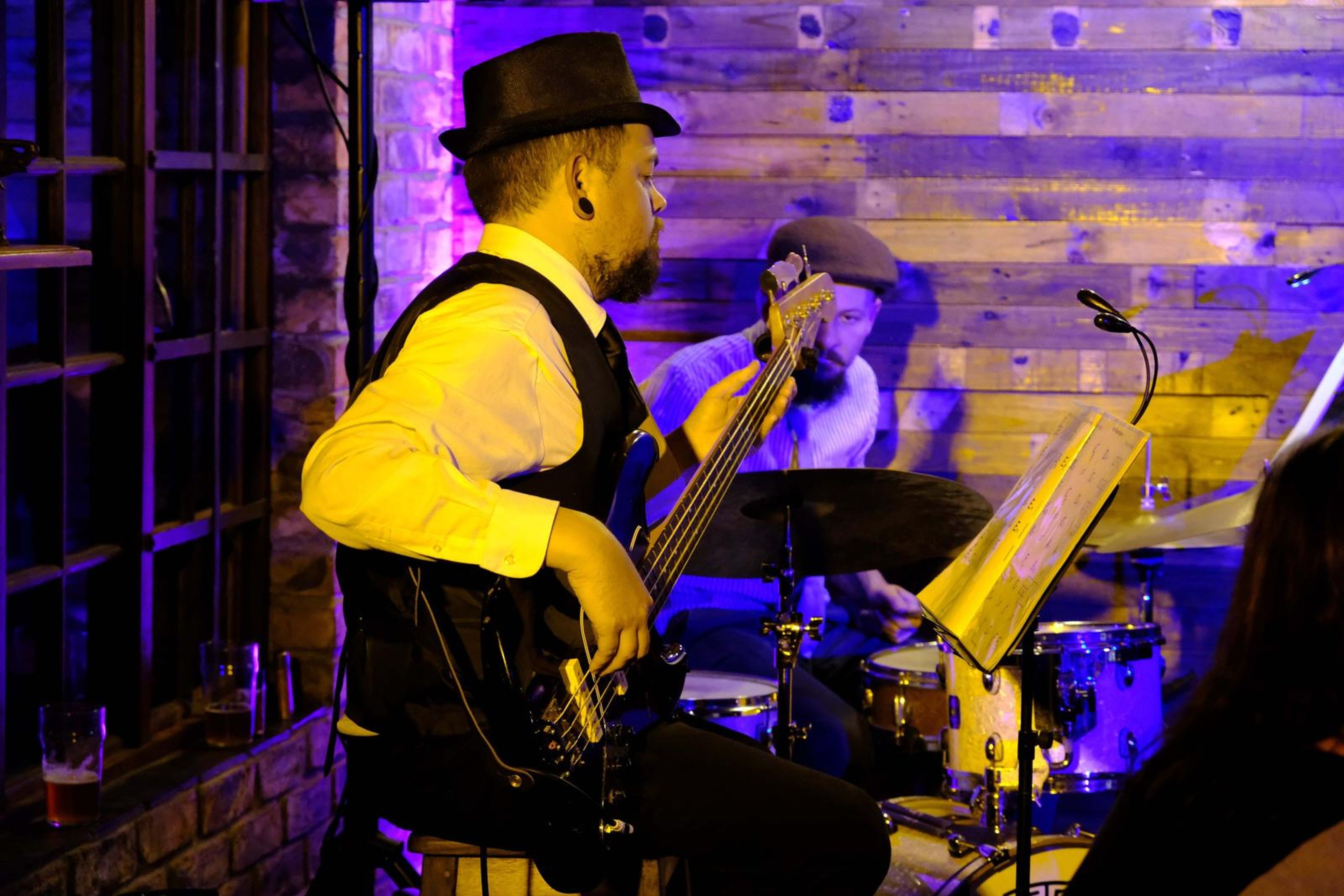 Bassist in a hat and waistcoat playing against a purple-lit wall