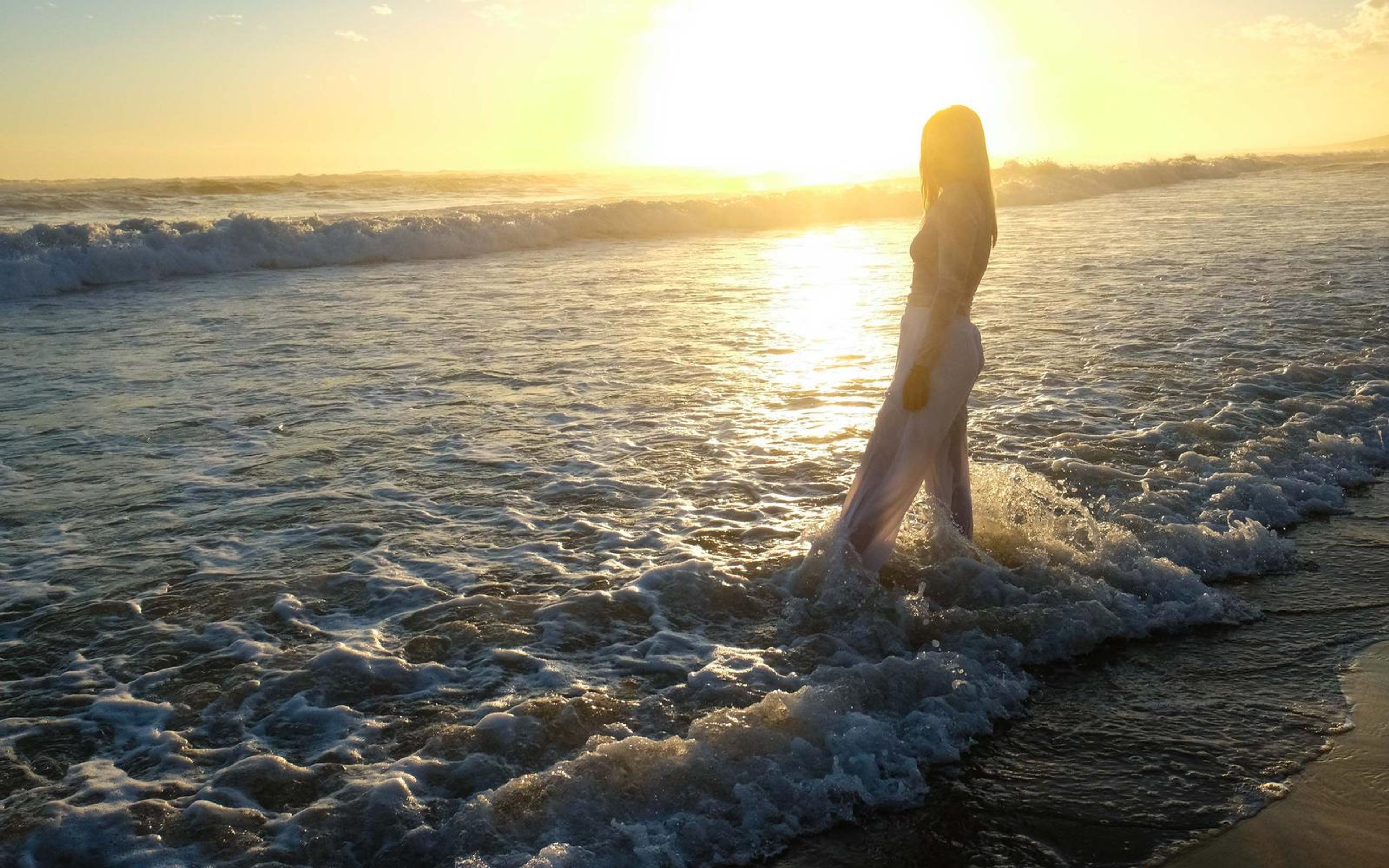 Figure walking into breaking waves with the low sun behind, wide silhouette view