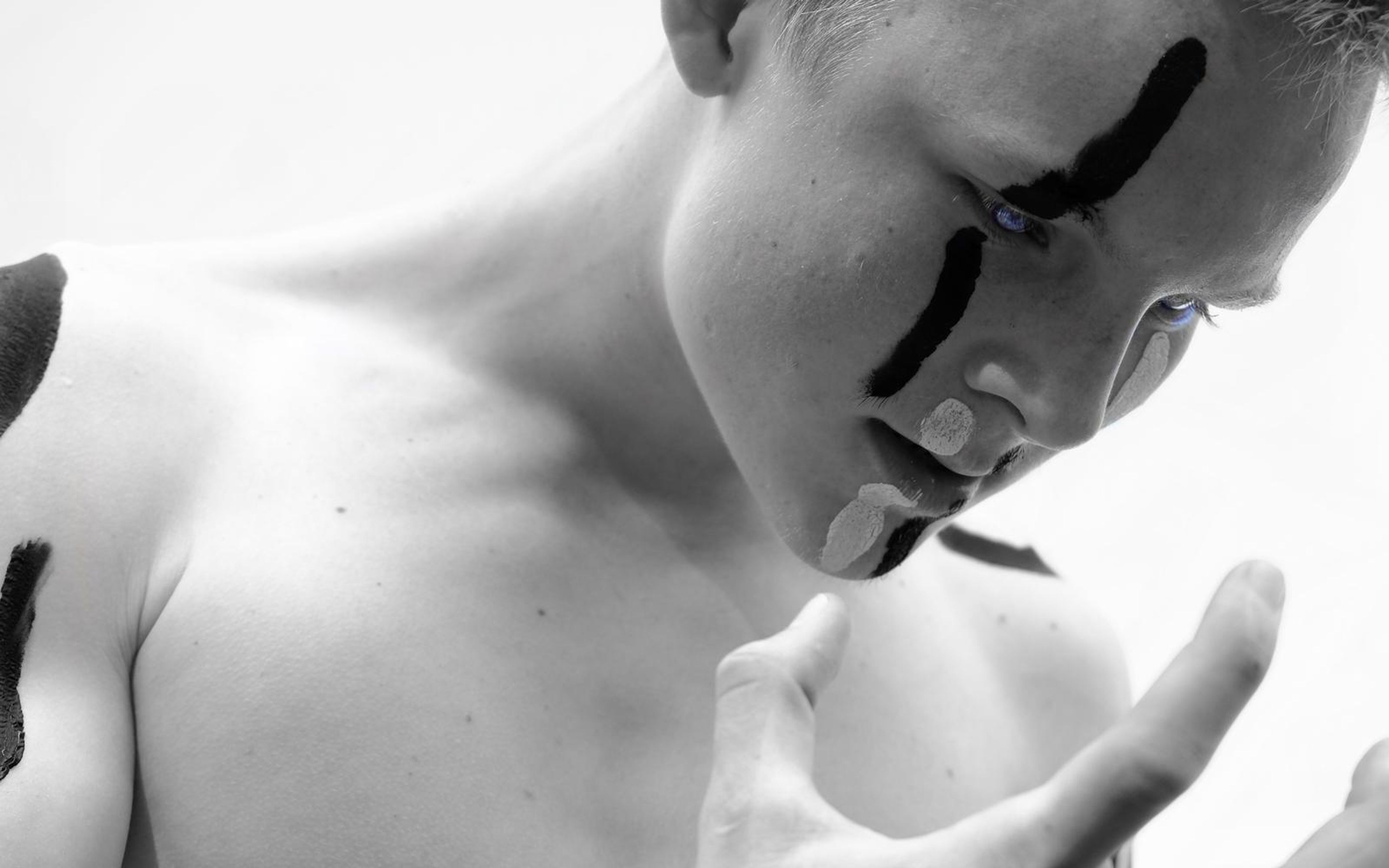 Soft black and white version of the performer looking down with painted streaks on the cheek and a hand curled in front