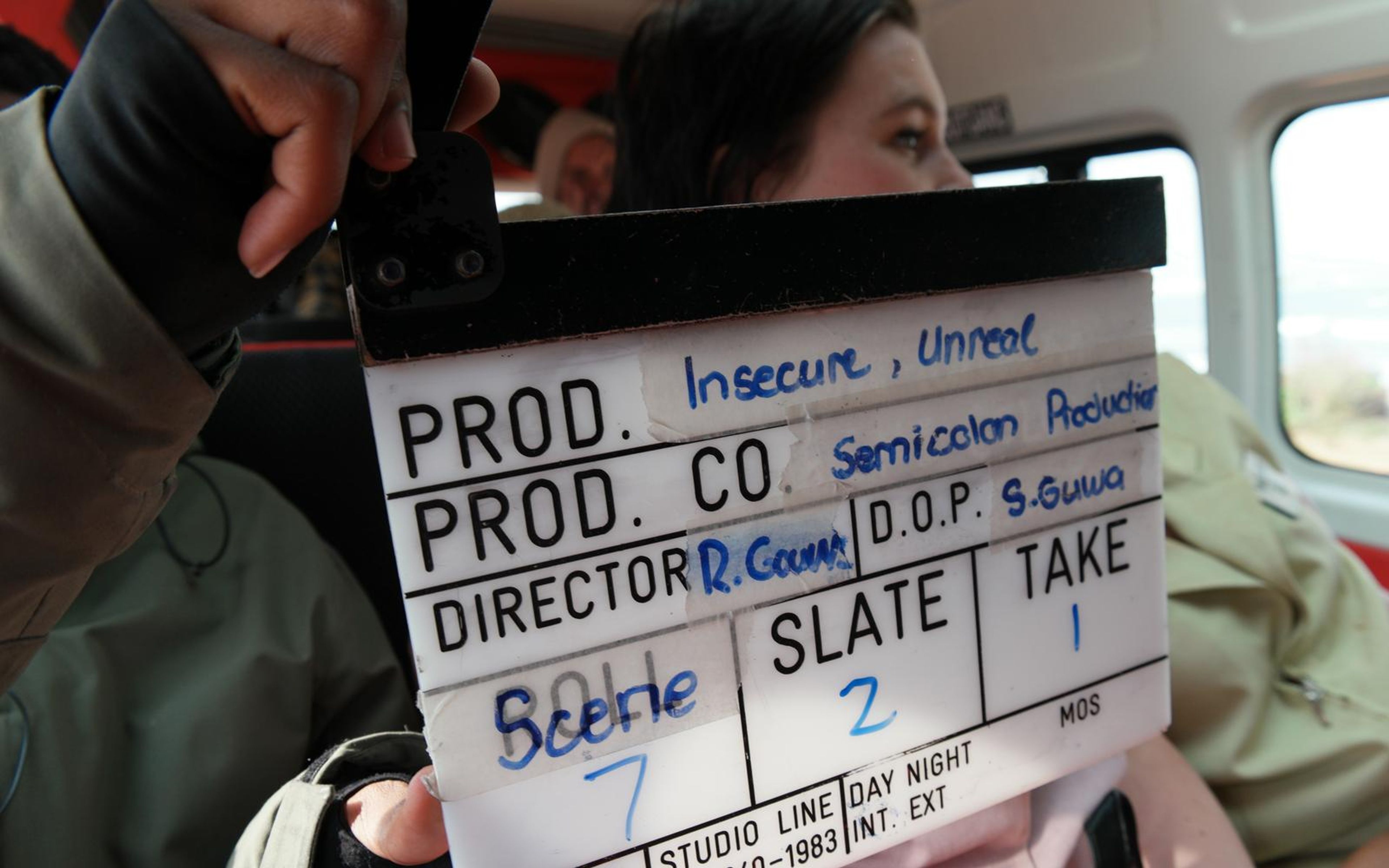 Clapperboard held in front of the camera inside a van, the production title written on the slate