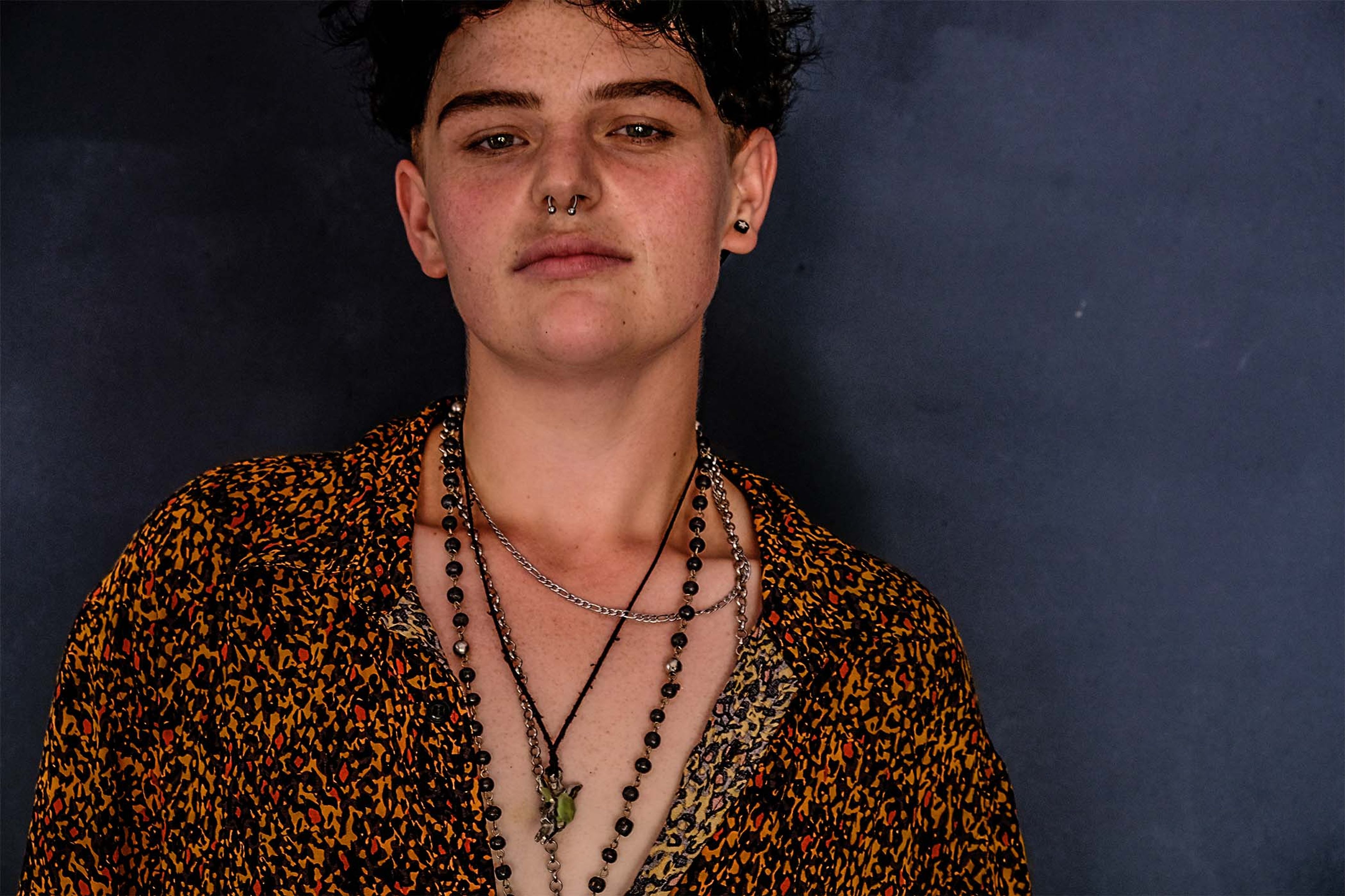 Portrait, subject in a patterned shirt with layered necklaces, direct gaze