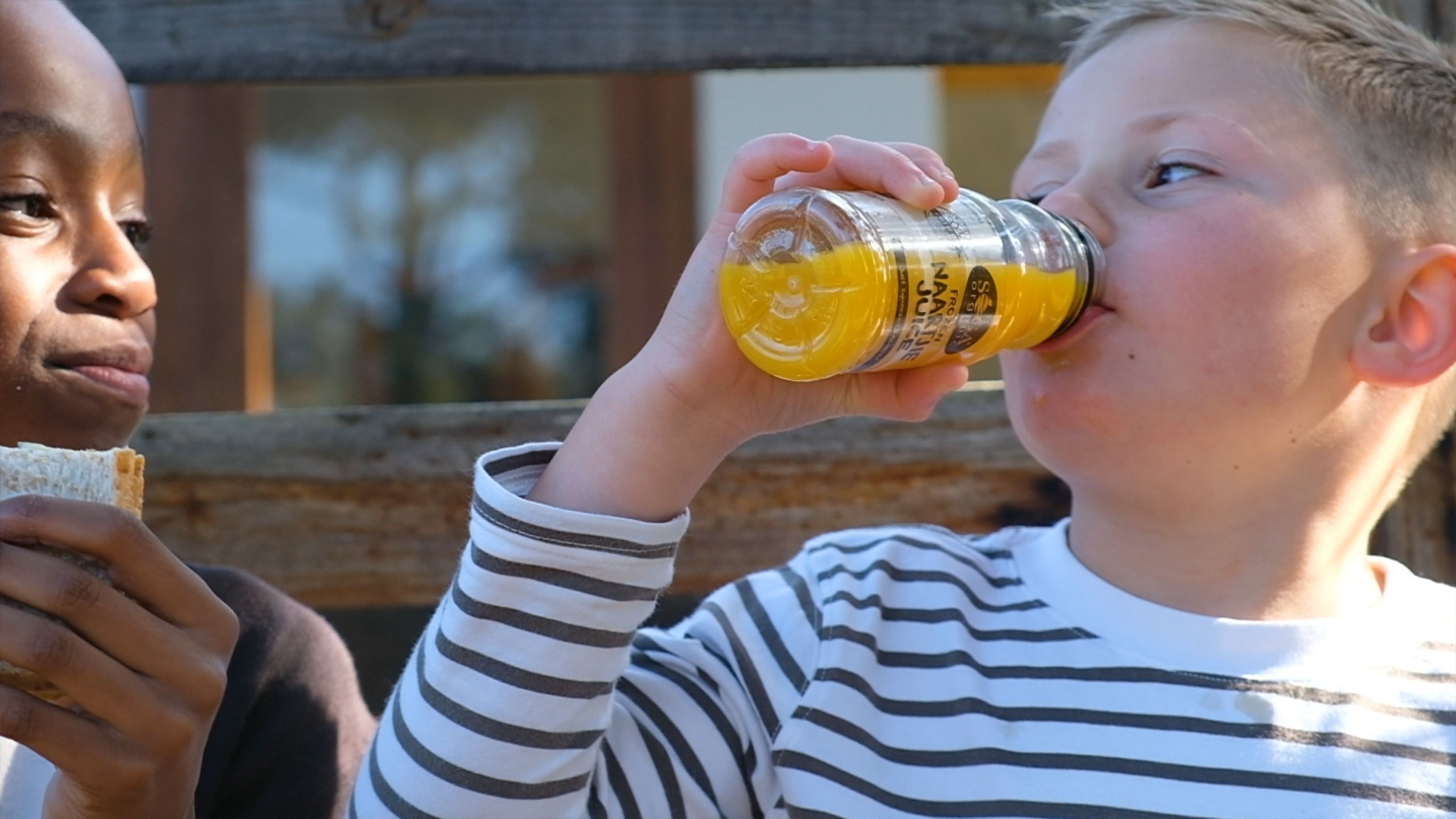 Boy drinking from a SOGA juice bottle with another child beside him