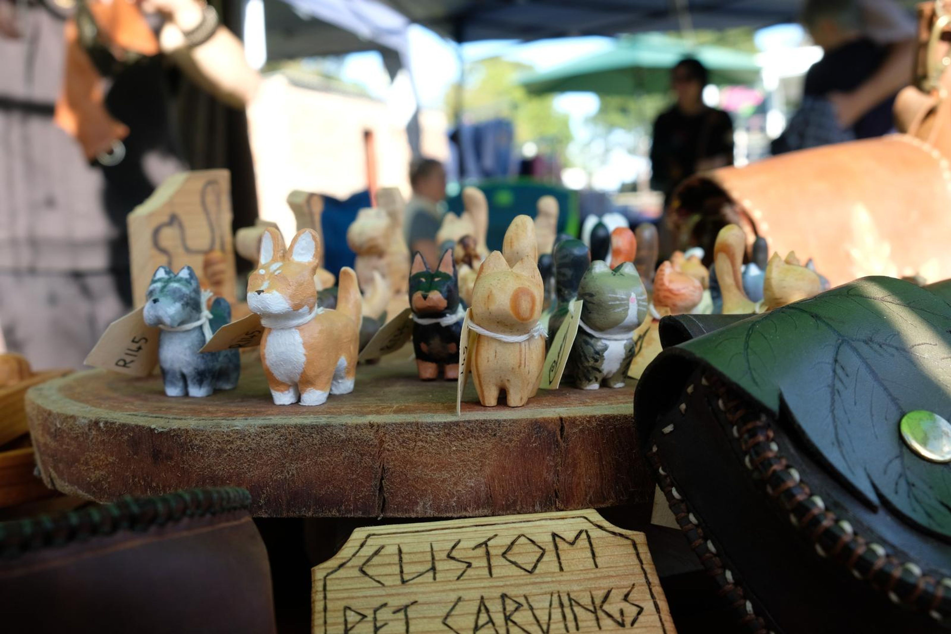Hand-carved wooden pet figures beside a Custom Pet Carvings sign and leaf pouch
