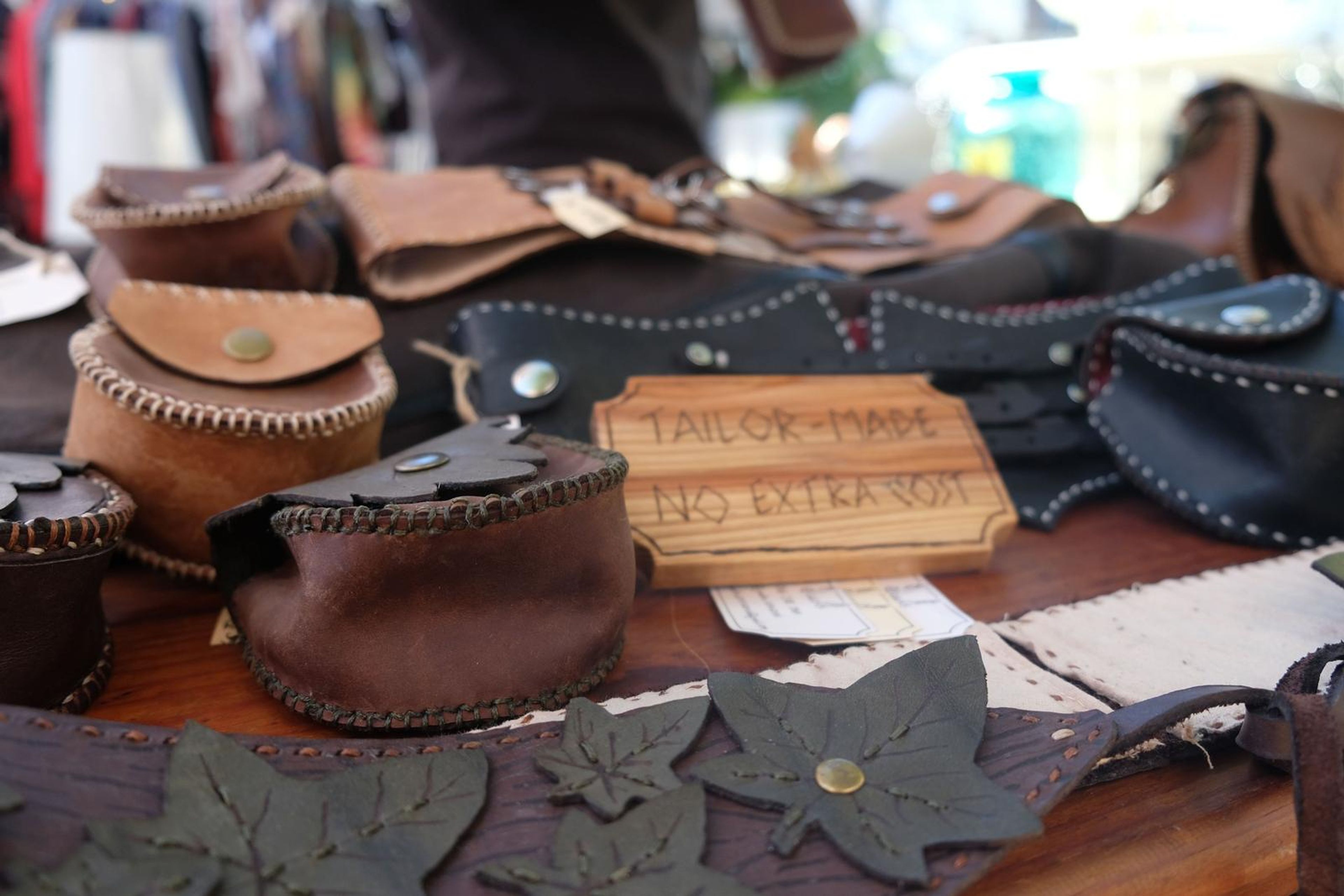 Table of handmade leather pouches and corset belts with a Tailor-Made No Extra Cost sign