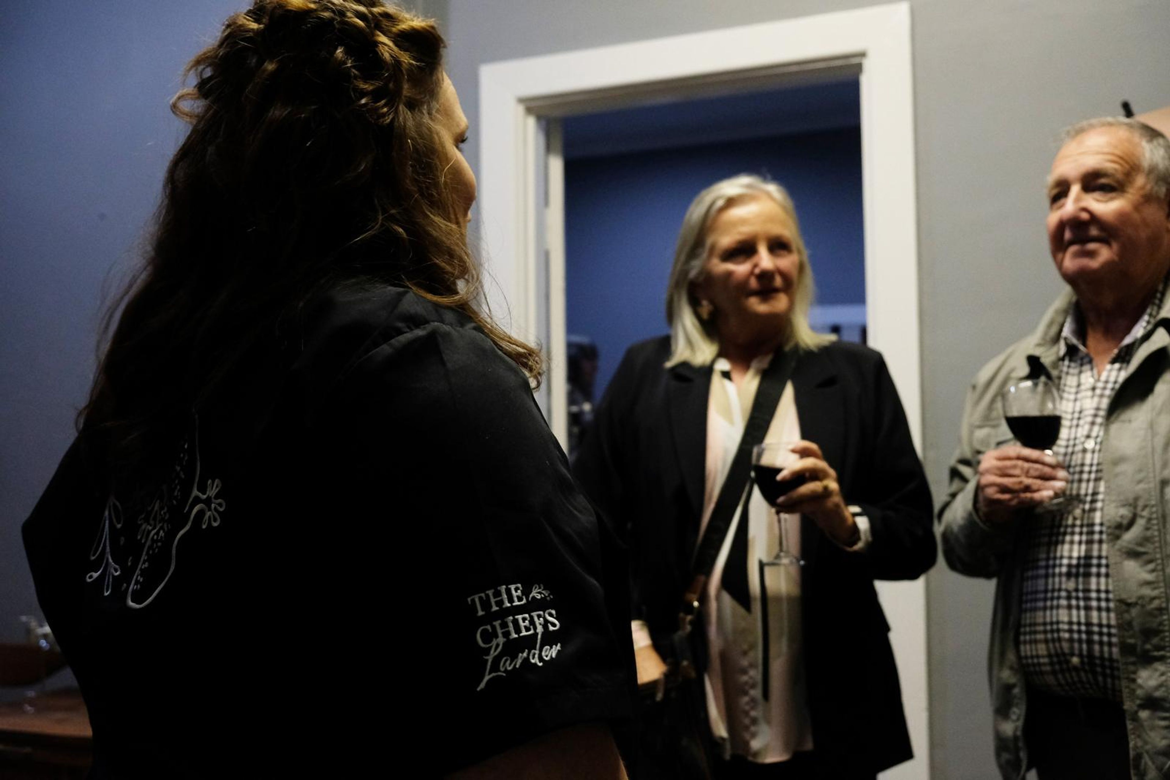 Chef in a Chef's Larder shirt talking with two guests holding wine