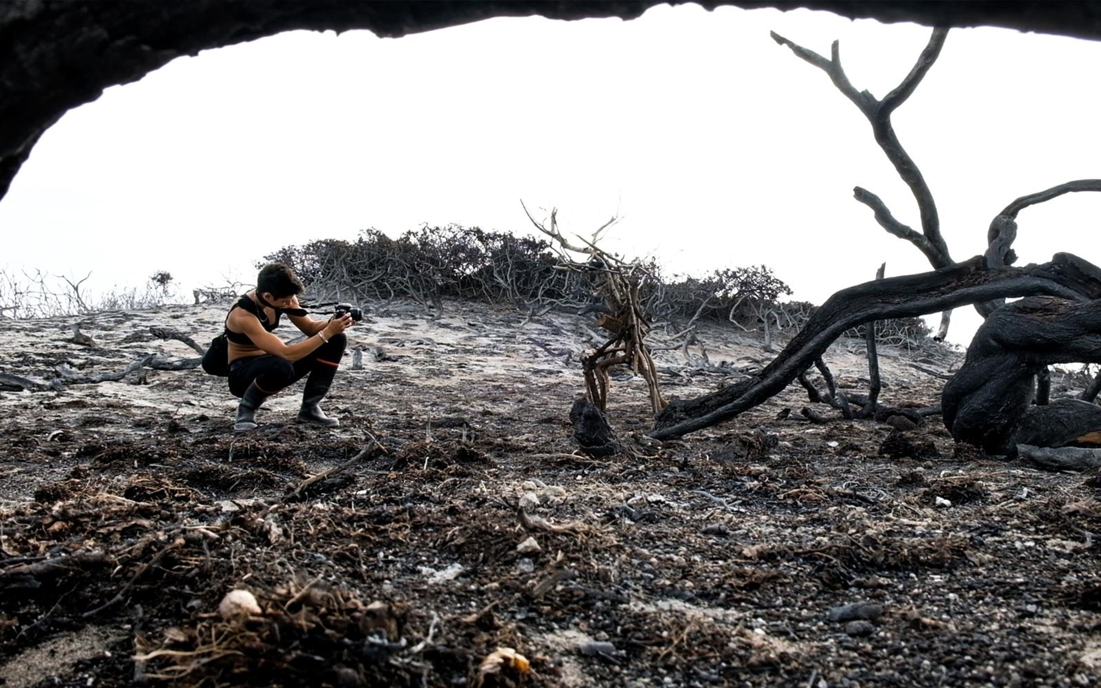 Person crouching to photograph, seen through a dark cave opening onto grey burnt ground