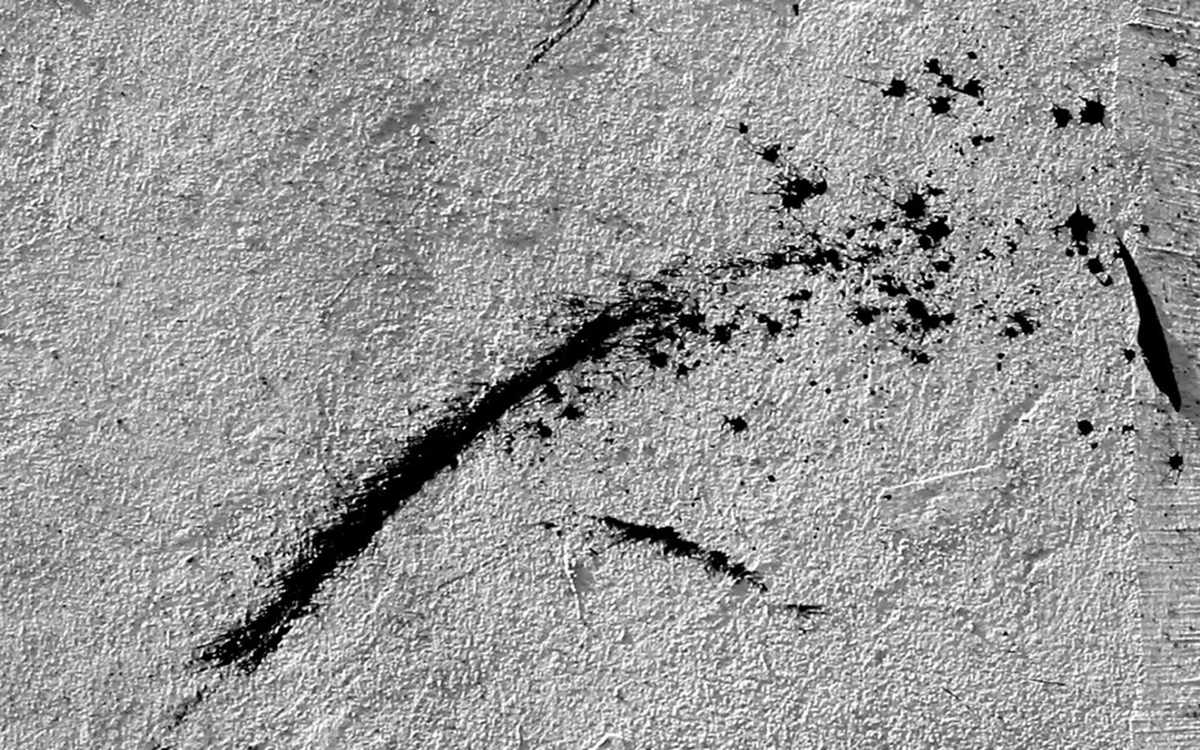Diagonal black ink streak and scattered splatter on grey textured concrete