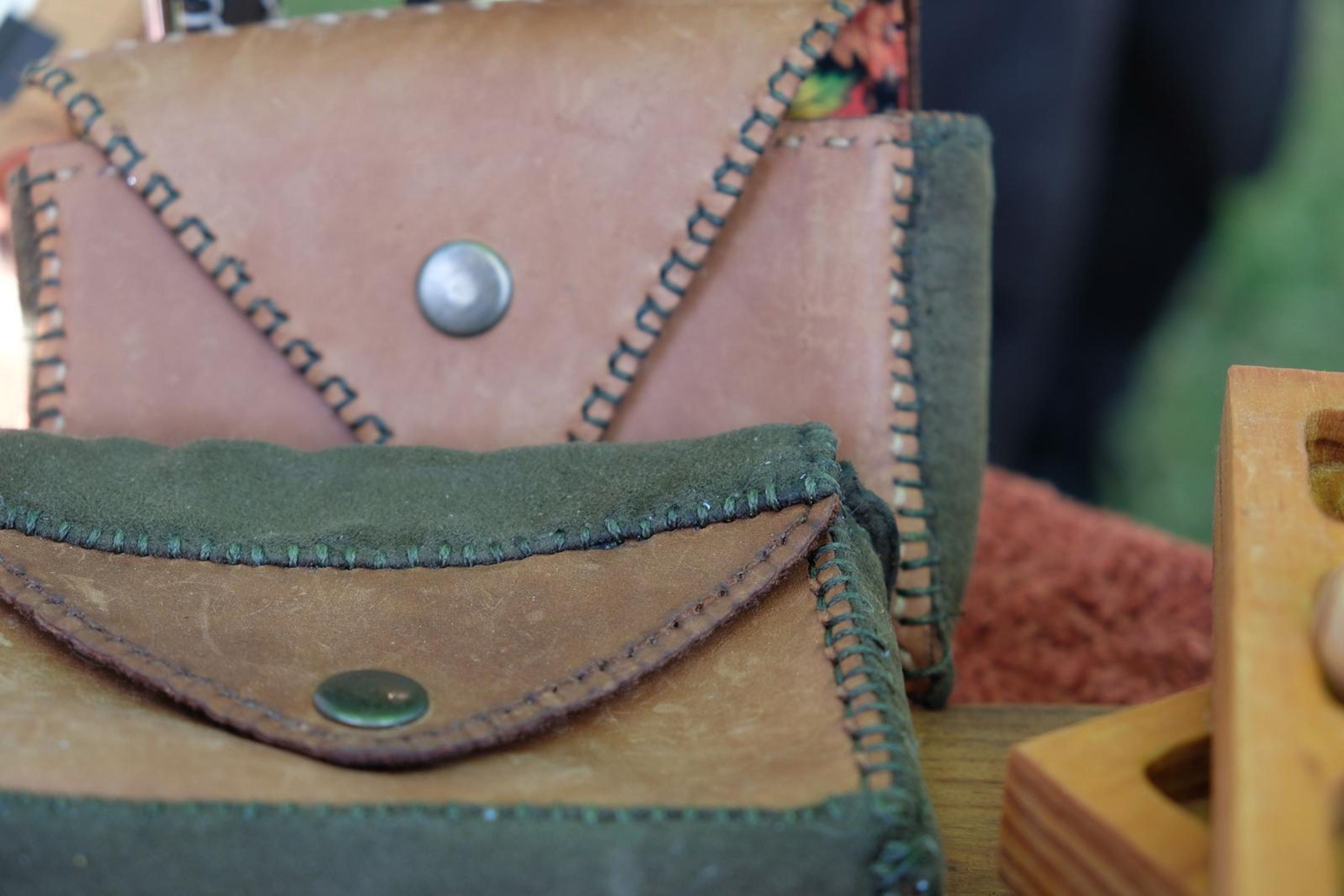 Two hand-stitched leather pouches in green and tan with metal studs