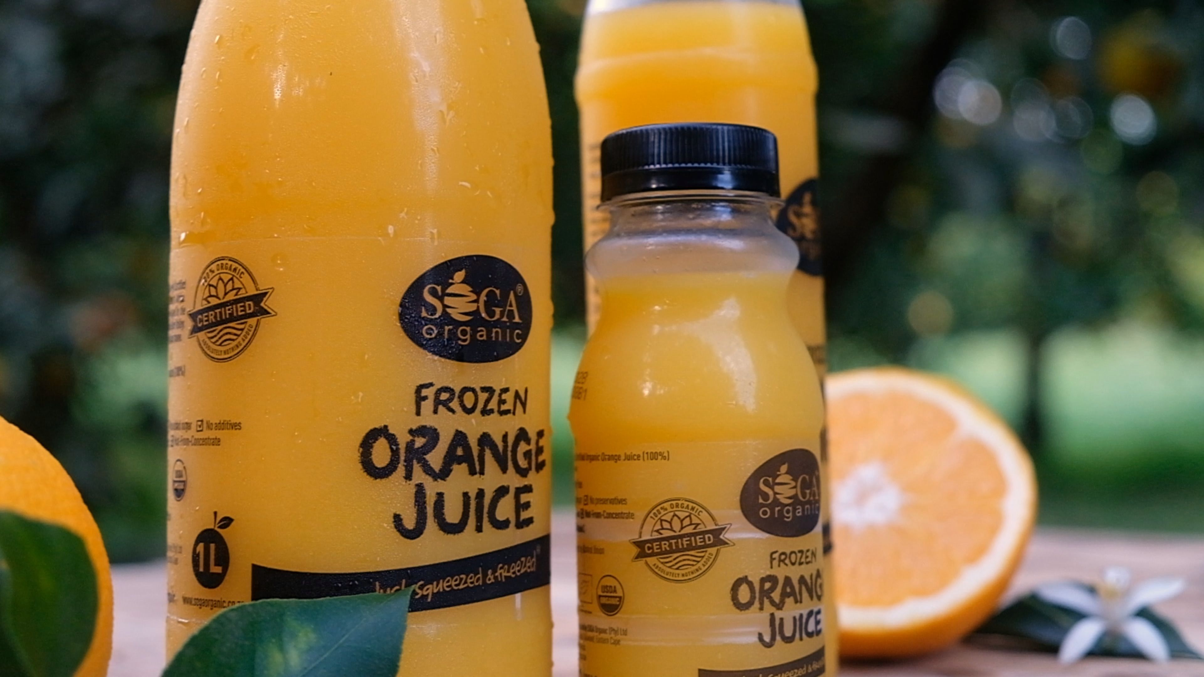 Close-up of SOGA Organic frozen orange juice bottles with orange halves behind them