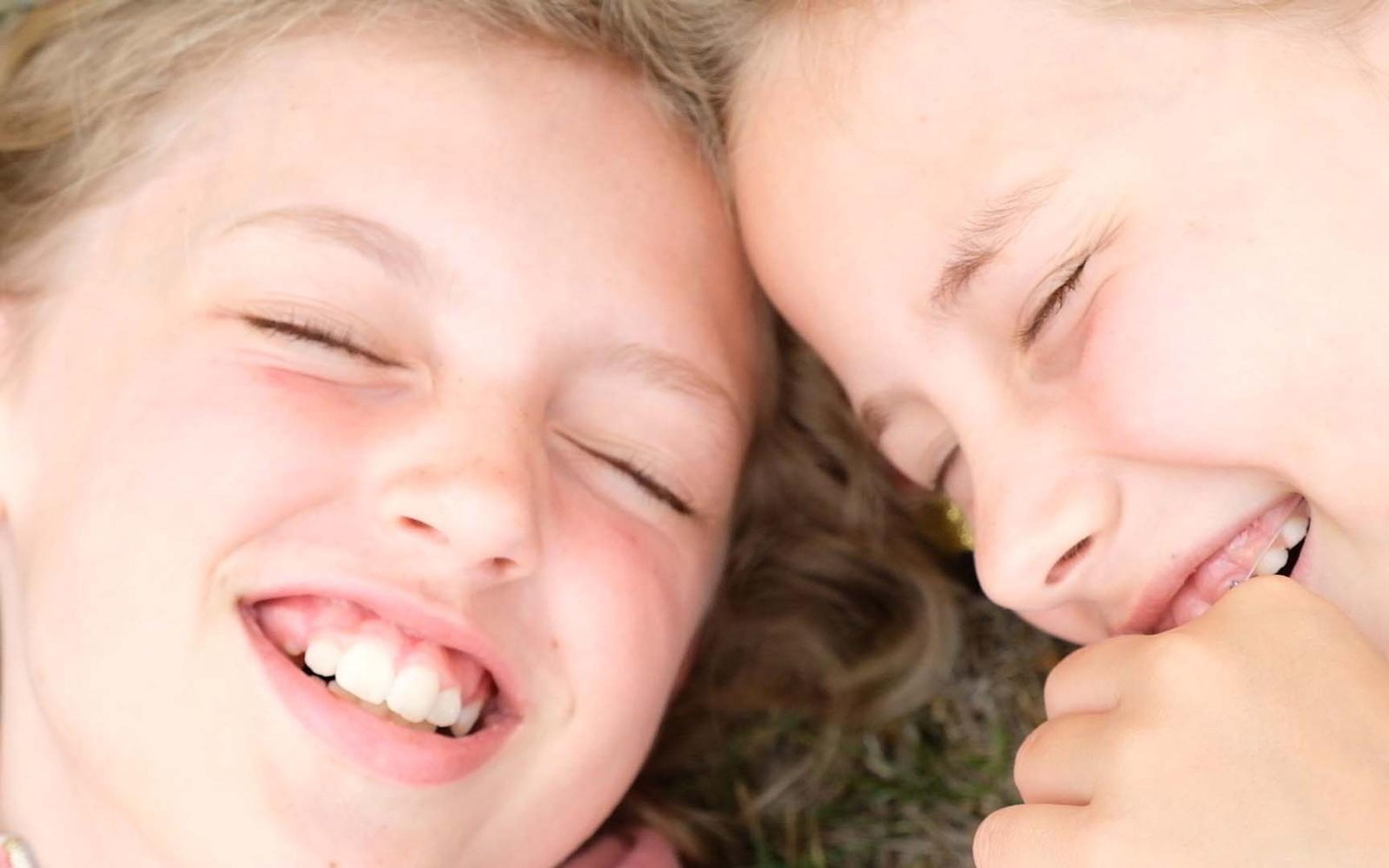 Two girls laughing with their heads together and eyes closed in close-up
